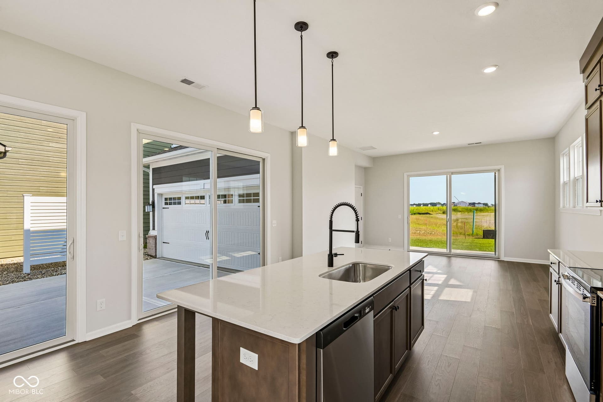 15691 Showdown Road, Noblesville, IN 46060 Open concept kitchen and living area featuring a central island with a stainless steel sink and matte black faucet, pendant lighting, wood-finish flooring, and two sliding glass doors