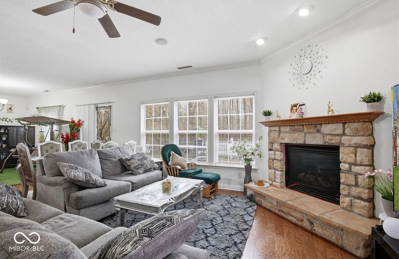 344 Legacy Boulevard, Greenwood, IN 46143 living area featuring crown molding, ceiling fan, a stone fireplace, and dark wood-type flooring