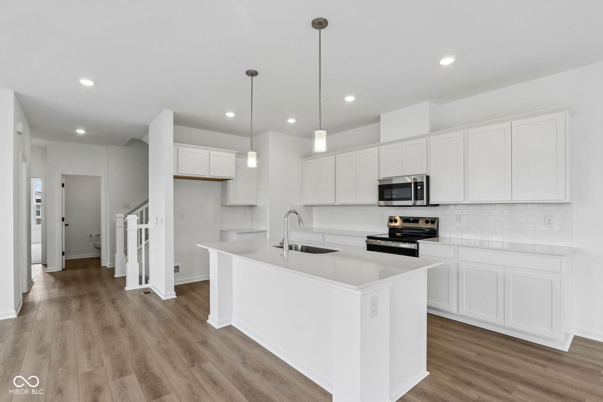 5748 Arcade Boulevard, McCordsville, IN 46055 Kitchen featuring an expansive island with an undermount sink, white cabinetry, integrated stainless steel appliances, and wood-finish flooring