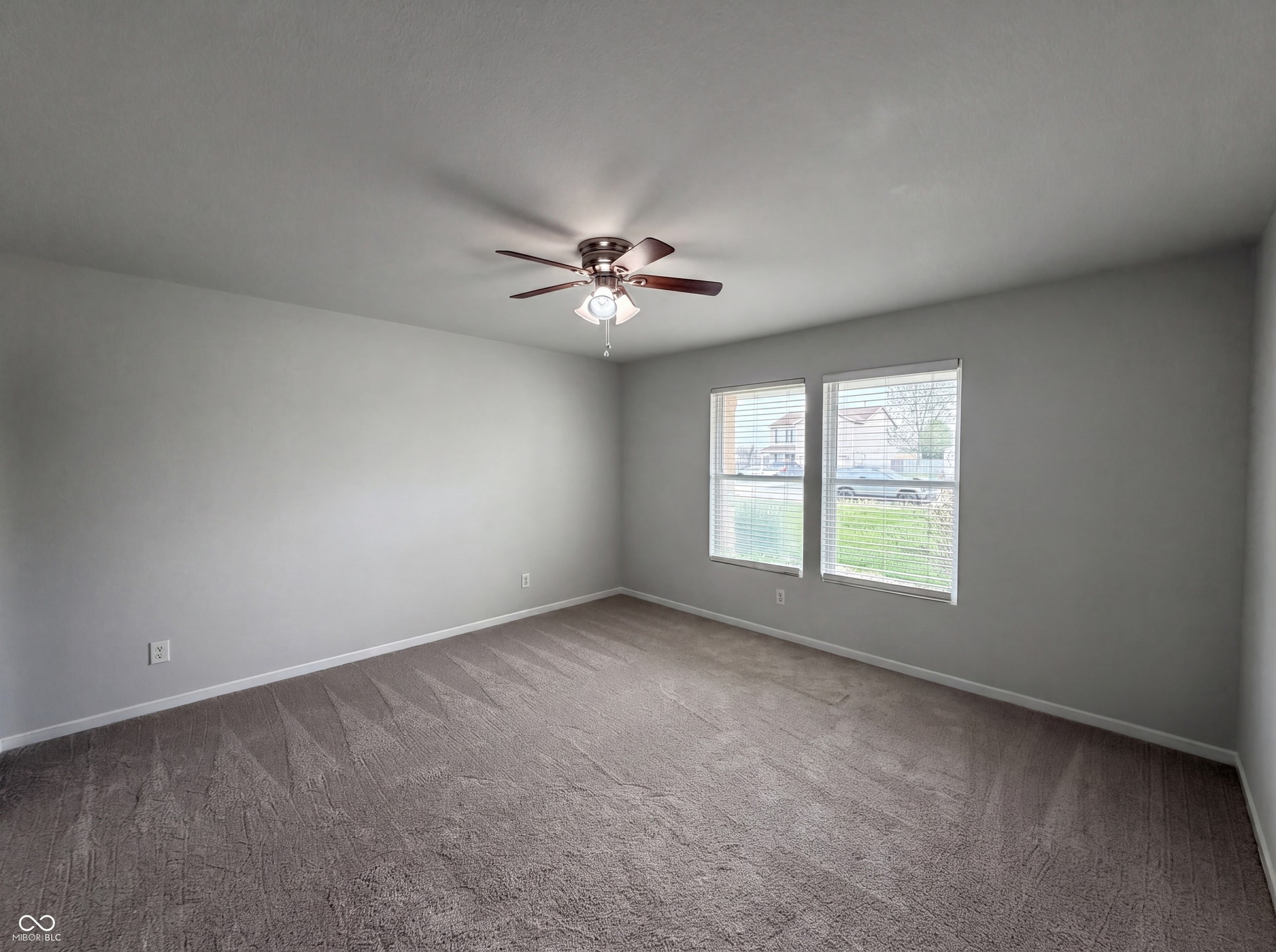 526 Bourneside Drive, Greenfield, IN 46140 Spacious room featuring neutral carpeting, light gray wall finishes, dual windows with blinds, and a ceiling fan with integrated lighting