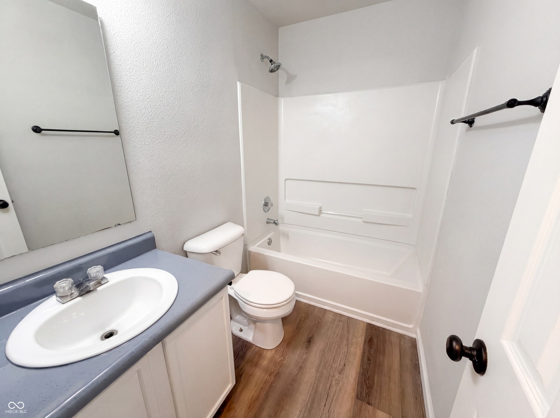 526 Bourneside Drive, Greenfield, IN 46140 Bathroom featuring wood-finish flooring, a white vanity with a blue countertop and integrated sink, a large wall-mounted mirror, a toilet, and a white bathtub with a shower and integrated shelving