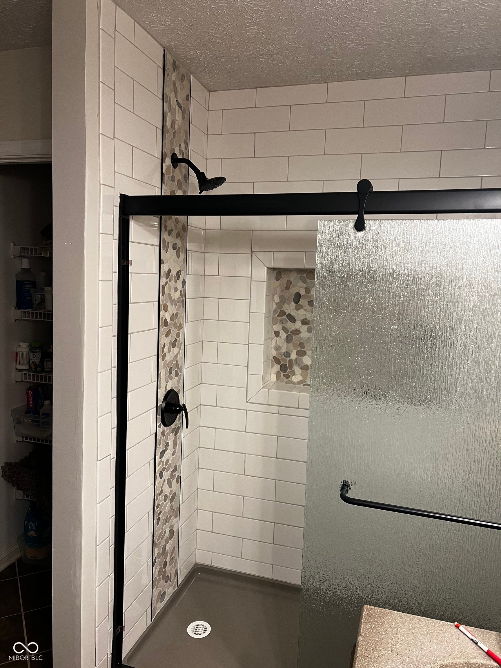 2117 Witt Road, Lebanon, IN 46052 Shower enclosure with white subway tile, pebble tile accents, matte black fixtures, integrated shower niche, and a textured glass sliding door
