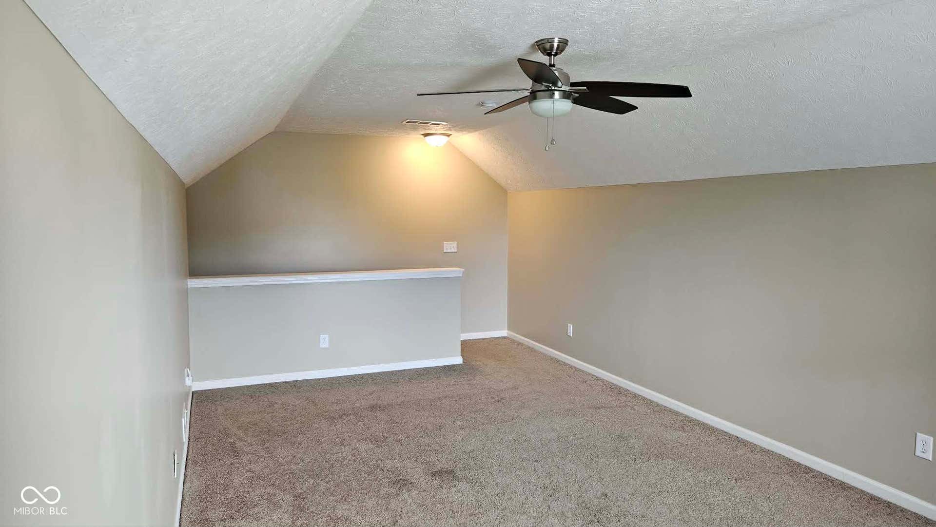 Loft space featuring sloped ceilings, textured wall finishes, and a ceiling fan with integrated lighting