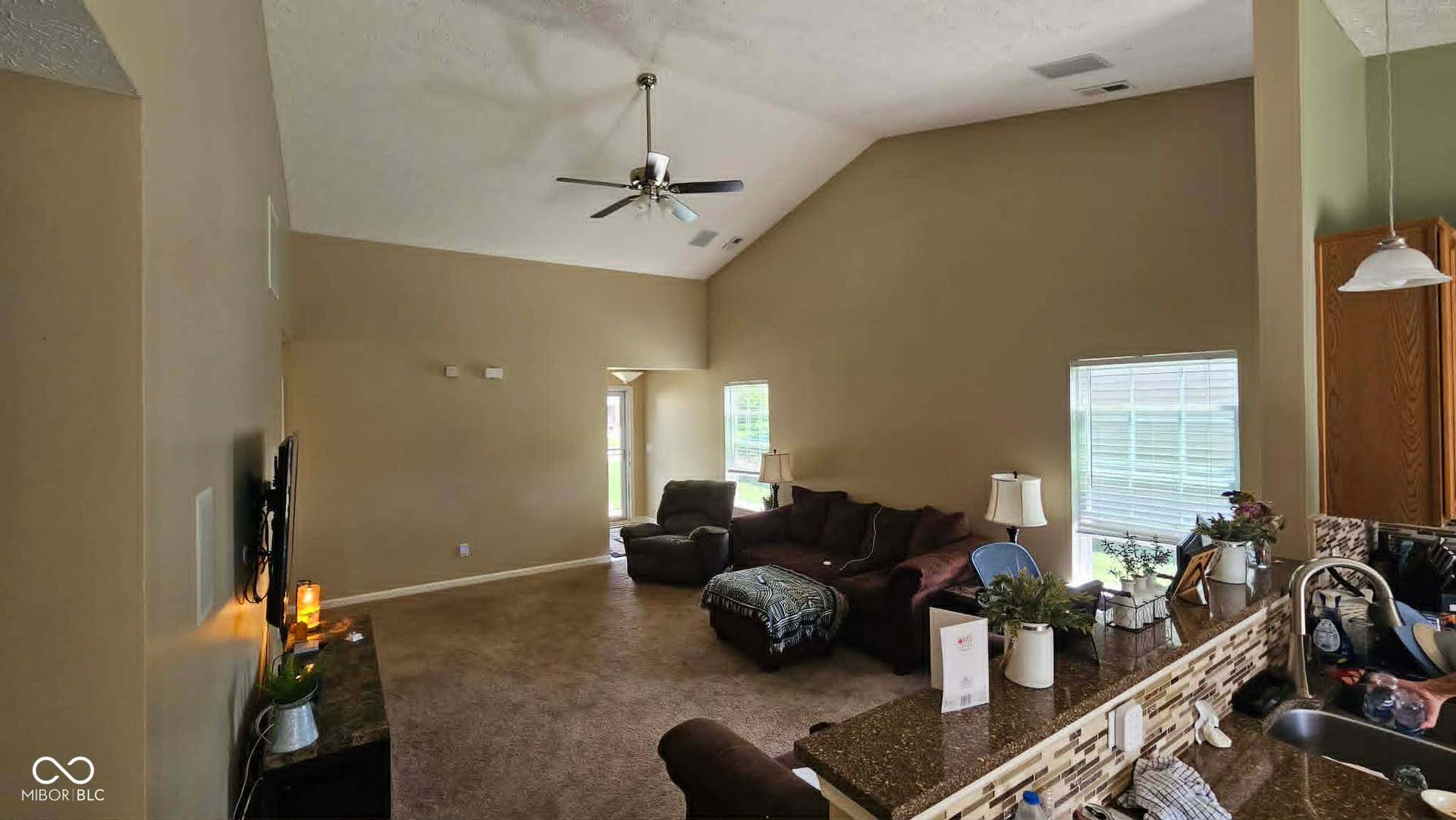 Living area featuring vaulted ceilings, a ceiling fan with light, and carpeted flooring