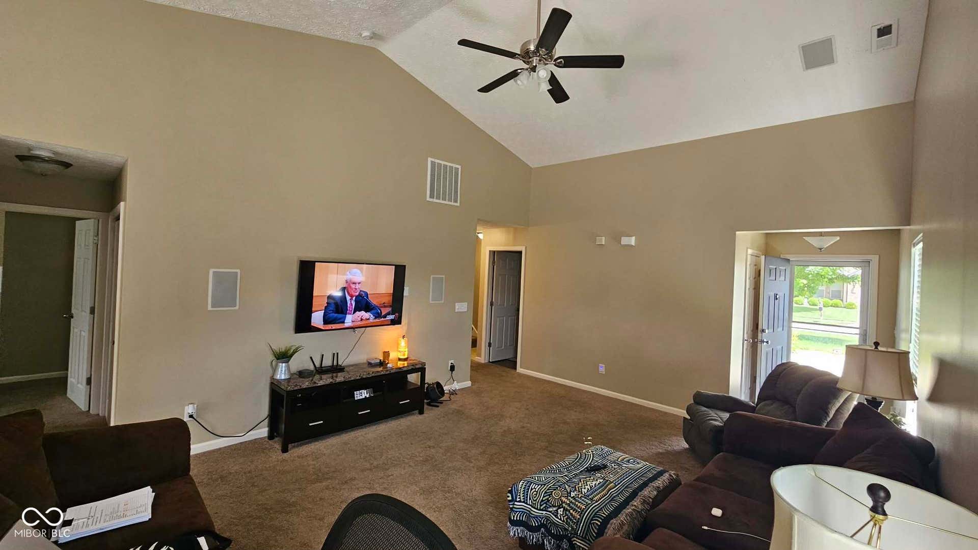 Living room featuring vaulted ceilings, a ceiling fan with integrated lighting, wall-mounted speakers, and recessed lighting