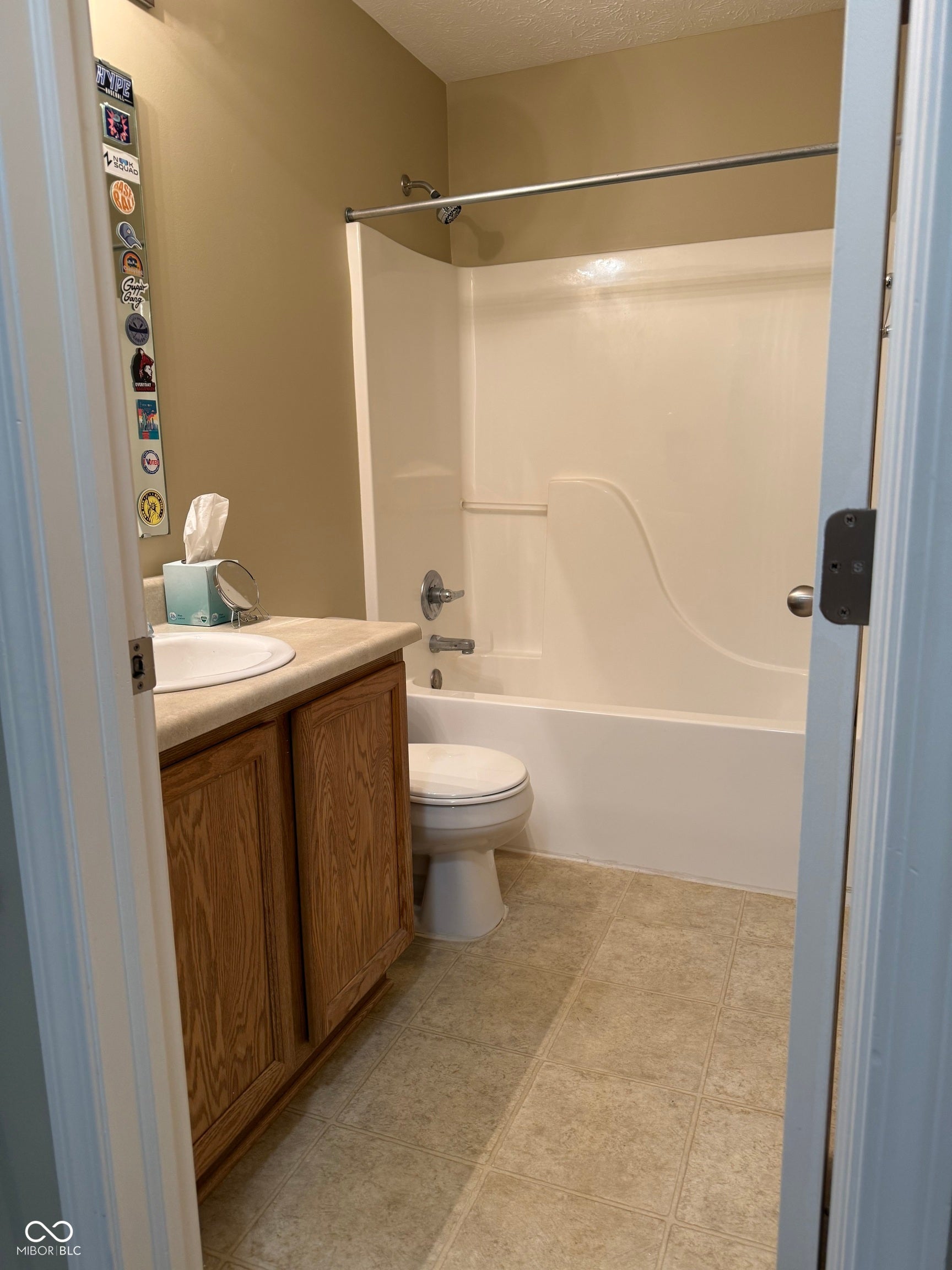 Full bathroom featuring a wood-finish vanity with integrated sink, ceramic tile flooring, toilet, and an alcove tub/shower combination with sliding glass enclosure and chrome fixtures