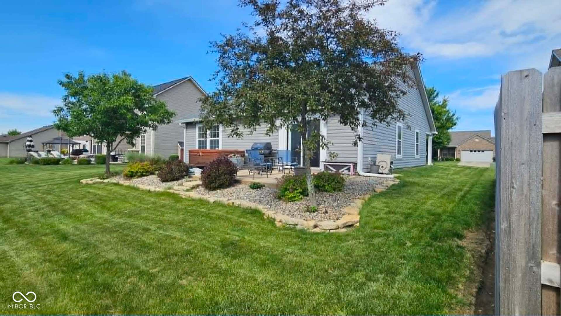 Expansive backyard featuring a stone patio, decorative landscaping with rock borders, and mature trees