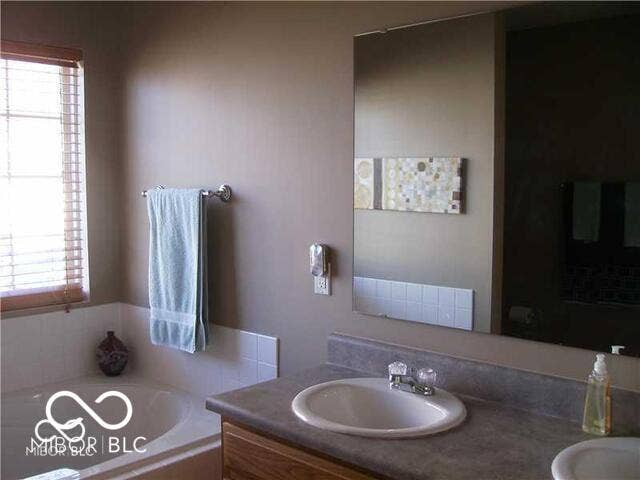 Bathroom featuring a built-in tub with white tile surround, a vanity with an integrated sink, and a large wall-mounted mirror