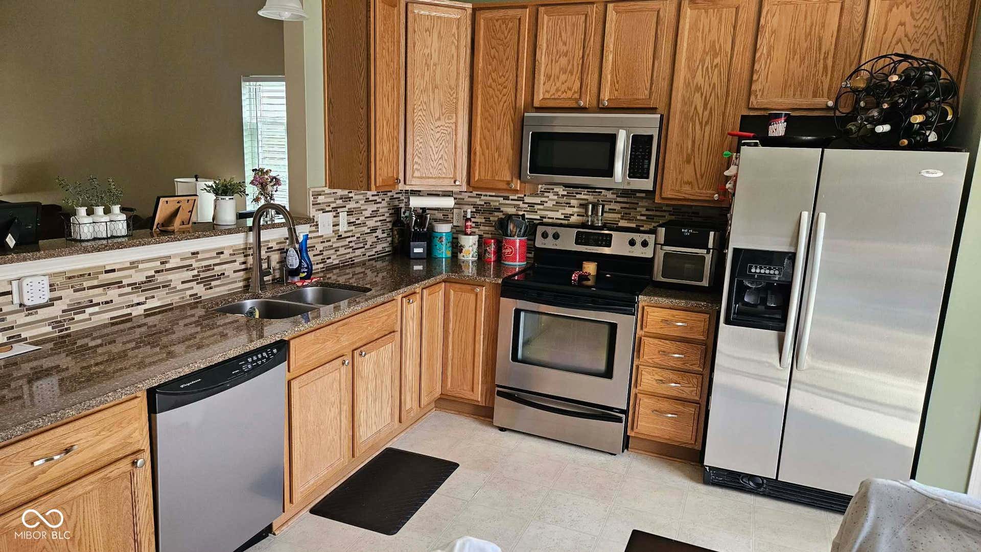 Kitchen featuring wood cabinetry, stainless steel appliances, a double basin sink, and a mosaic tile backsplash