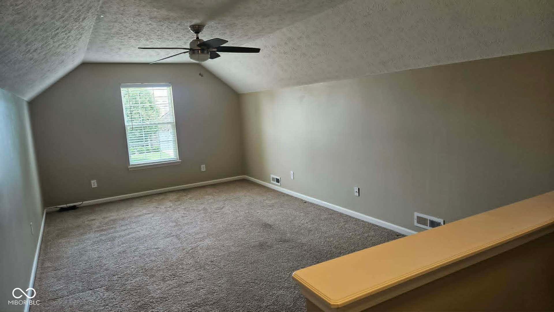 Loft features a vaulted ceiling with a ceiling fan, a window with blinds, and neutral wall tones with lots of room.
