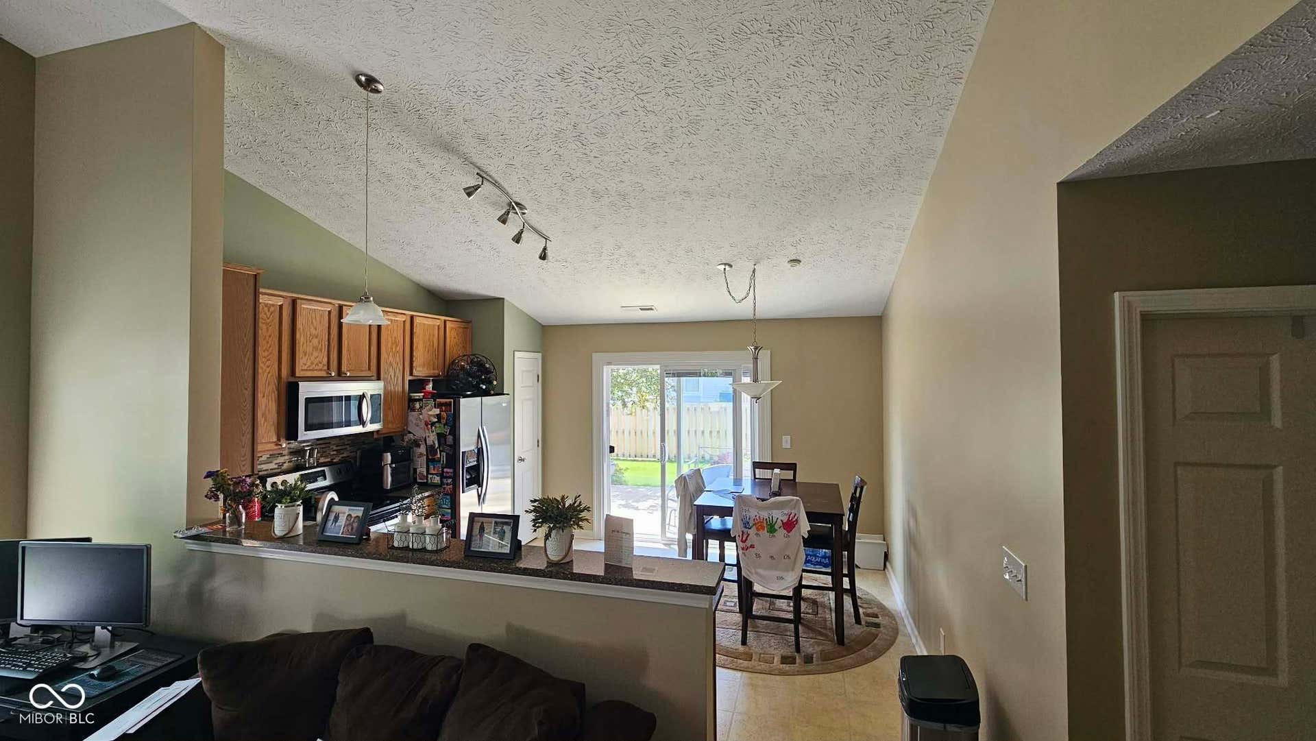 Vaulted ceiling kitchen and dining area featuring warm-toned cabinetry, stainless steel appliances, and track lighting