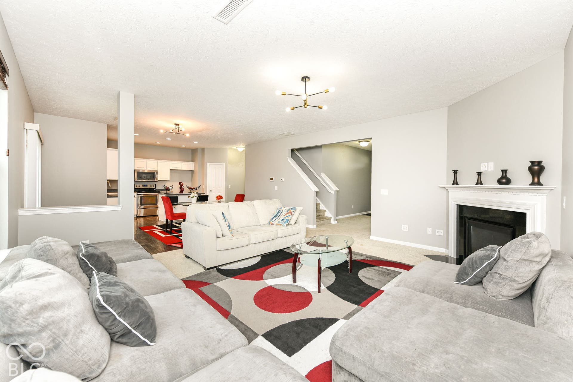 Living area with a modern chandelier, a white mantel, and a fireplace