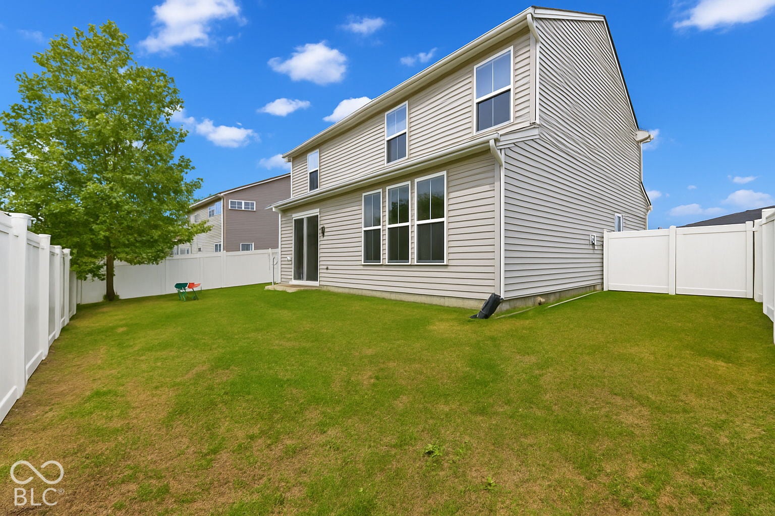 Rear exterior of the property featuring light-colored siding, multiple windows, and a sliding glass door