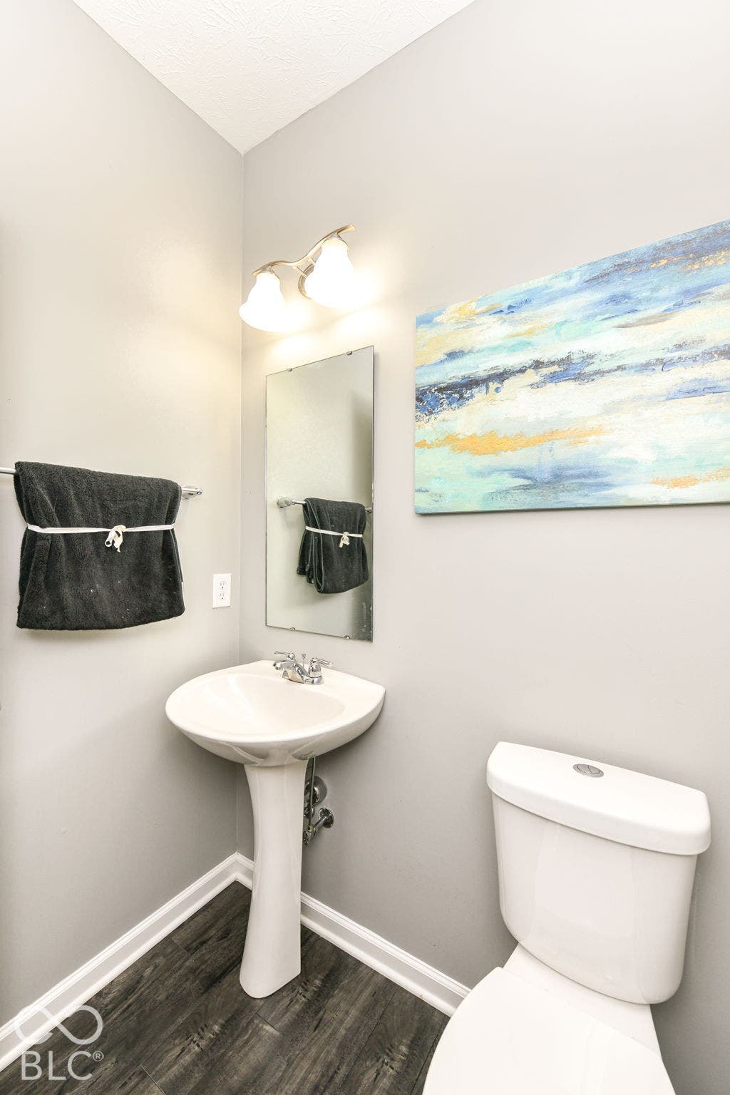 Pedestal sink with chrome fixtures, wood-finish flooring, wall-mounted mirror, and overhead lighting