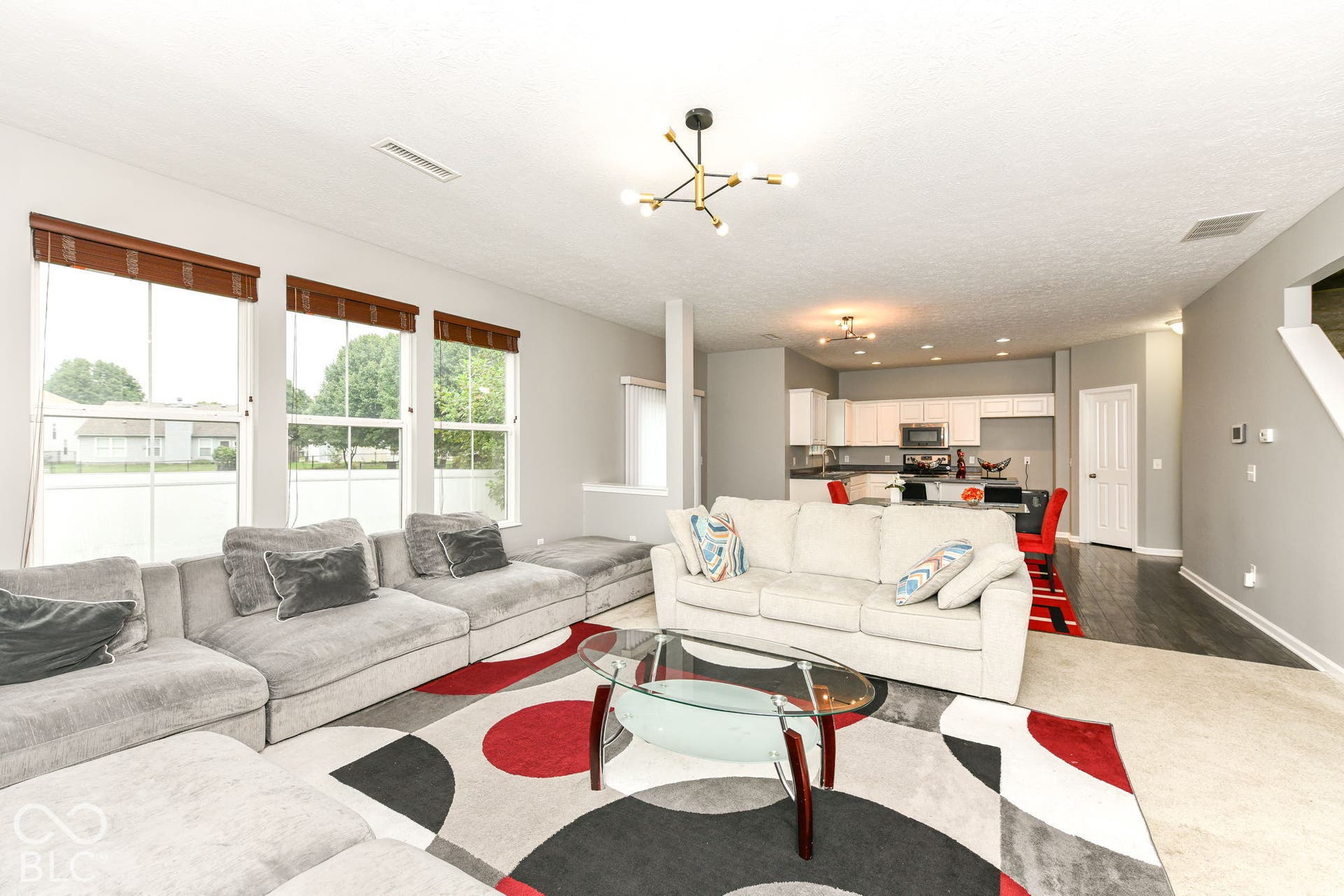 Open-concept living area with a contemporary chandelier, multiple windows, and a kitchen featuring white cabinetry and dark countertops