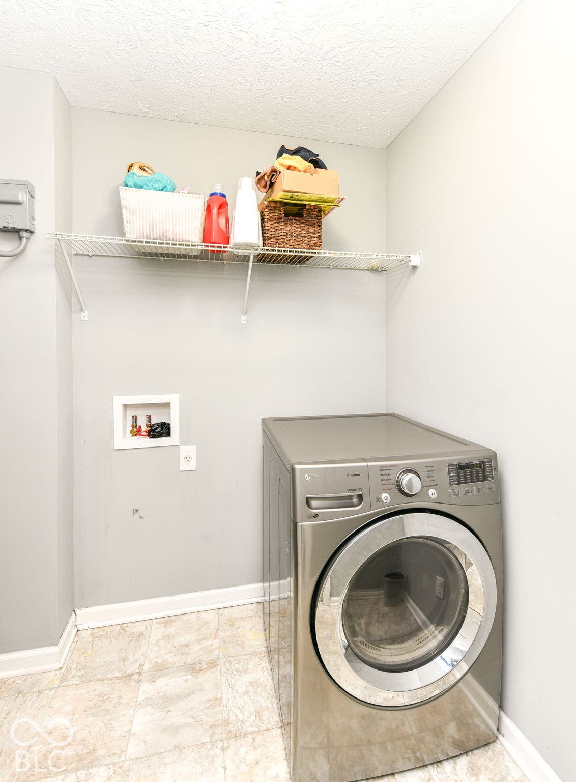Laundry area featuring neutral wall paint, a wire shelf, and tile flooring