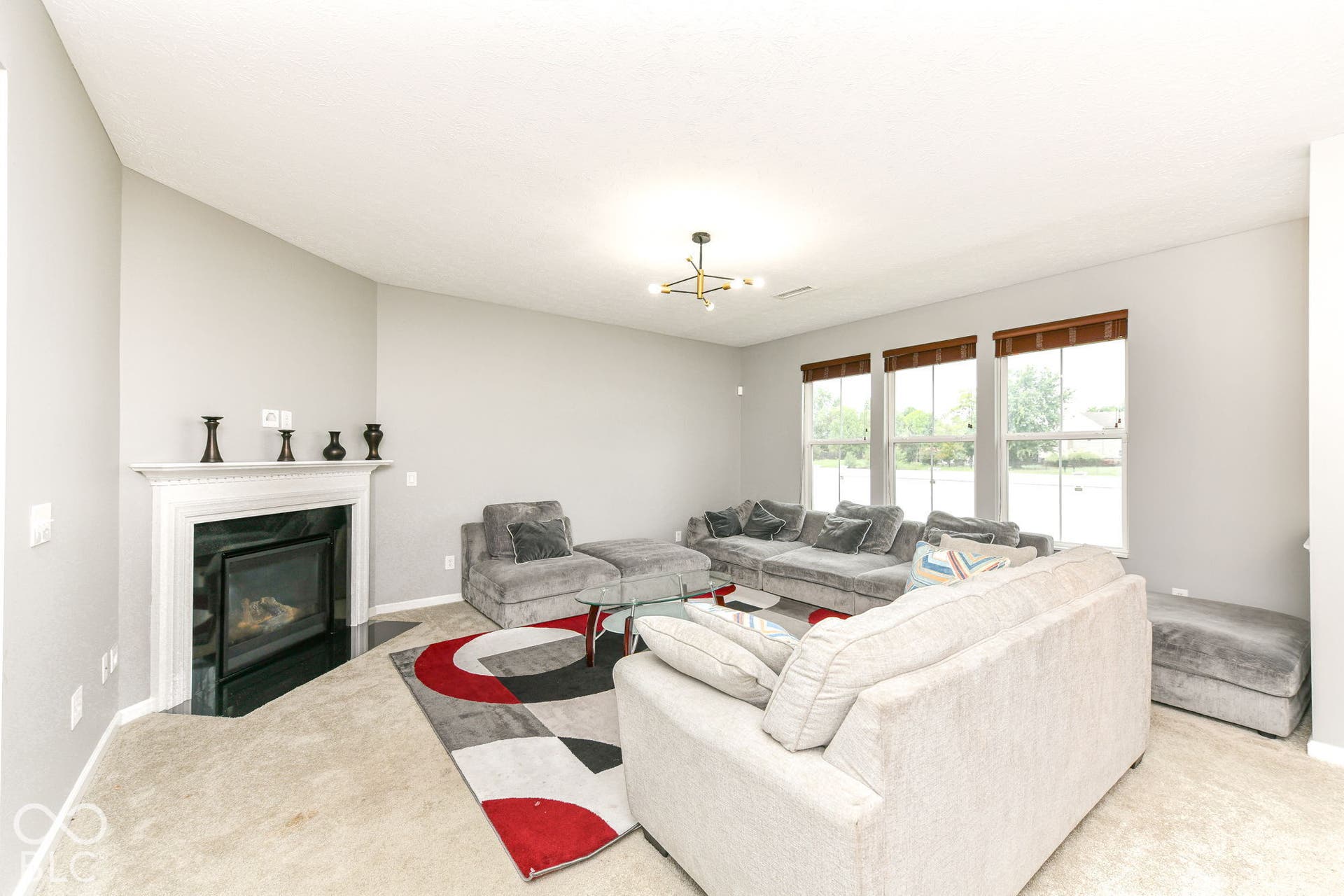 Living area featuring a fireplace with a white mantel, black surround, and three large windows with wood blinds