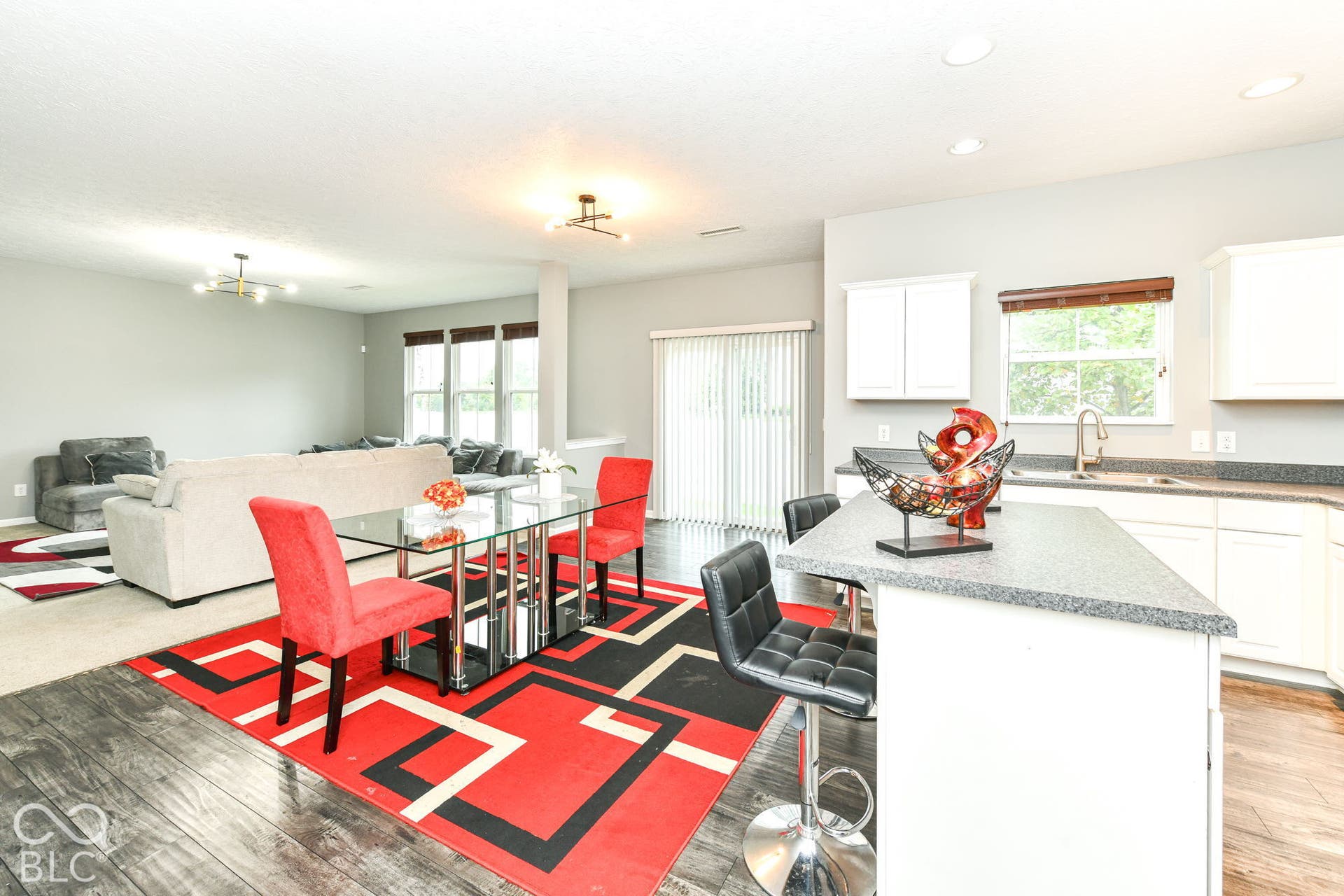 Open-concept living and dining area featuring wood-finish flooring, abundant natural light from multiple windows and glass doors, a chef's kitchen with white cabinetry and quartz countertops, and a large center island with seating