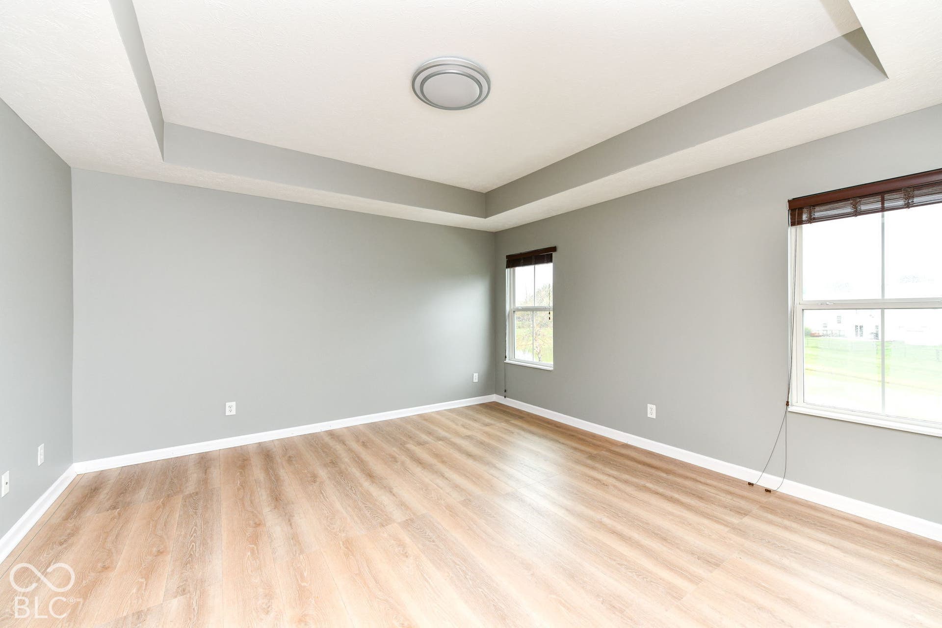 Tray ceiling with recessed lighting, wood-finish flooring, and multiple windows