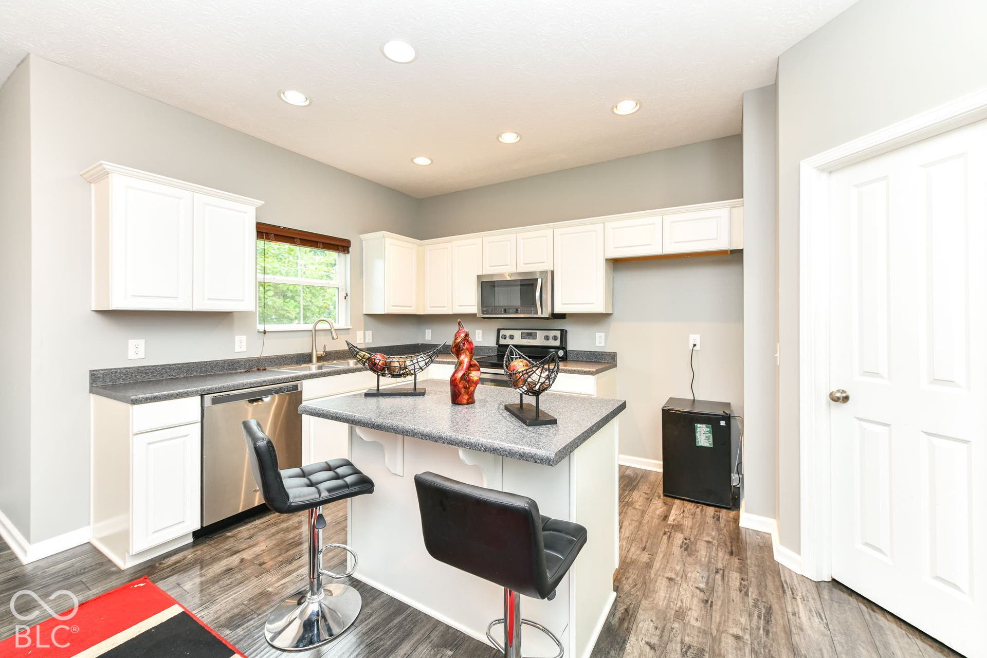 White shaker cabinetry, speckled countertops, stainless steel appliances, wood-finish flooring, and recessed lighting