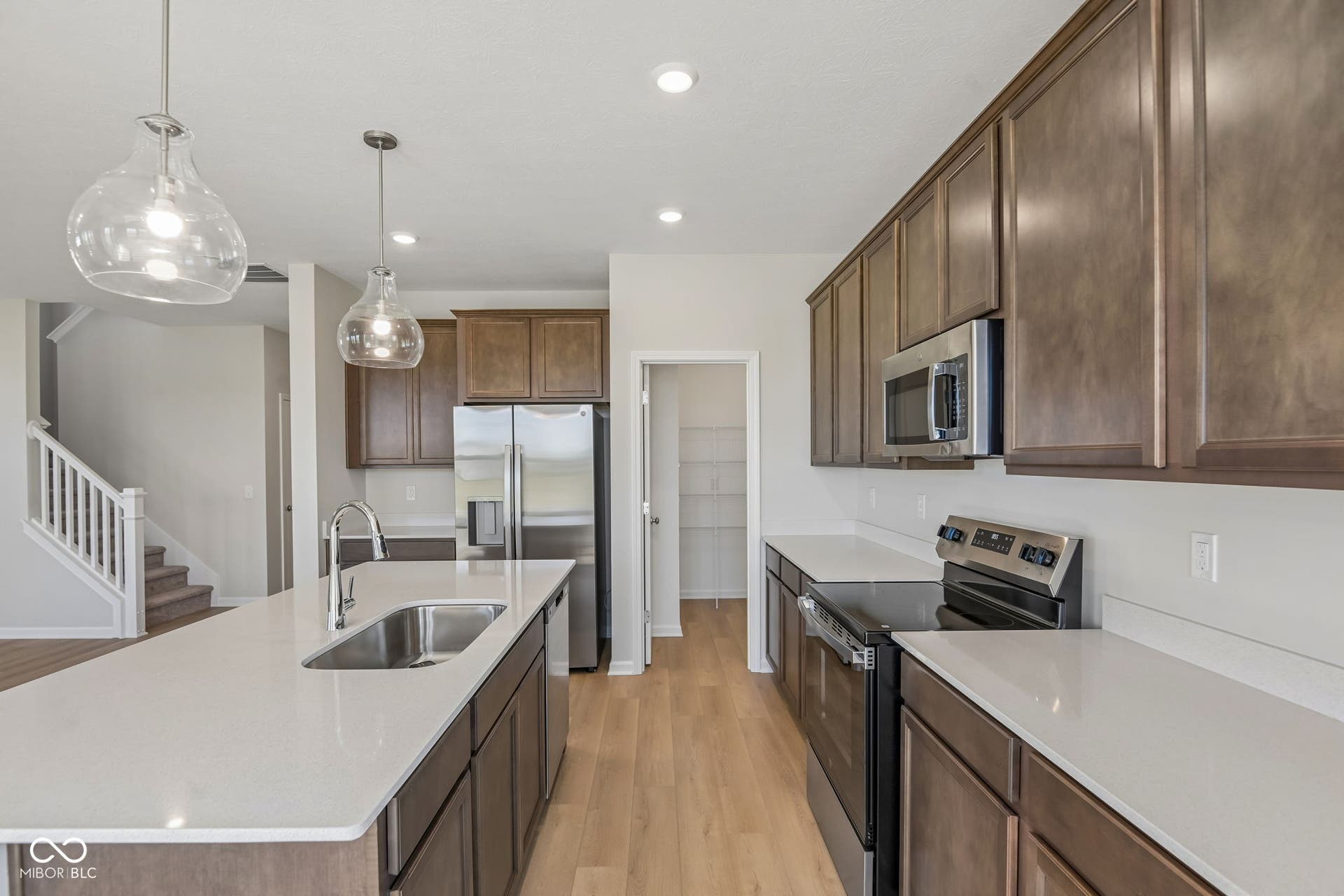 Kitchen featuring a central island with an undermount sink, pendant lighting, stainless steel appliances, and wood-finish flooring