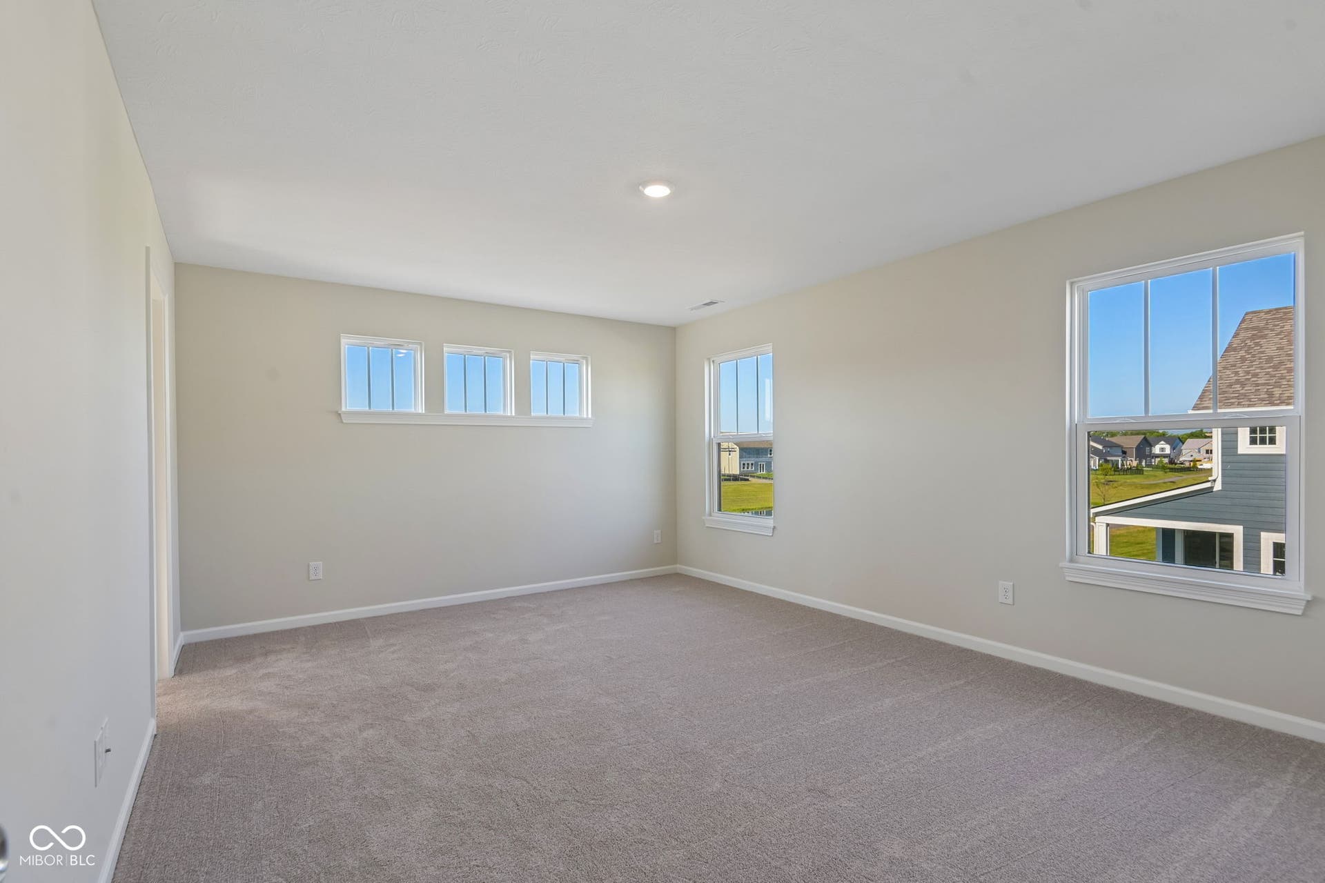 Spacious room featuring neutral carpeting, light-toned walls, recessed lighting, and multiple windows with white trim