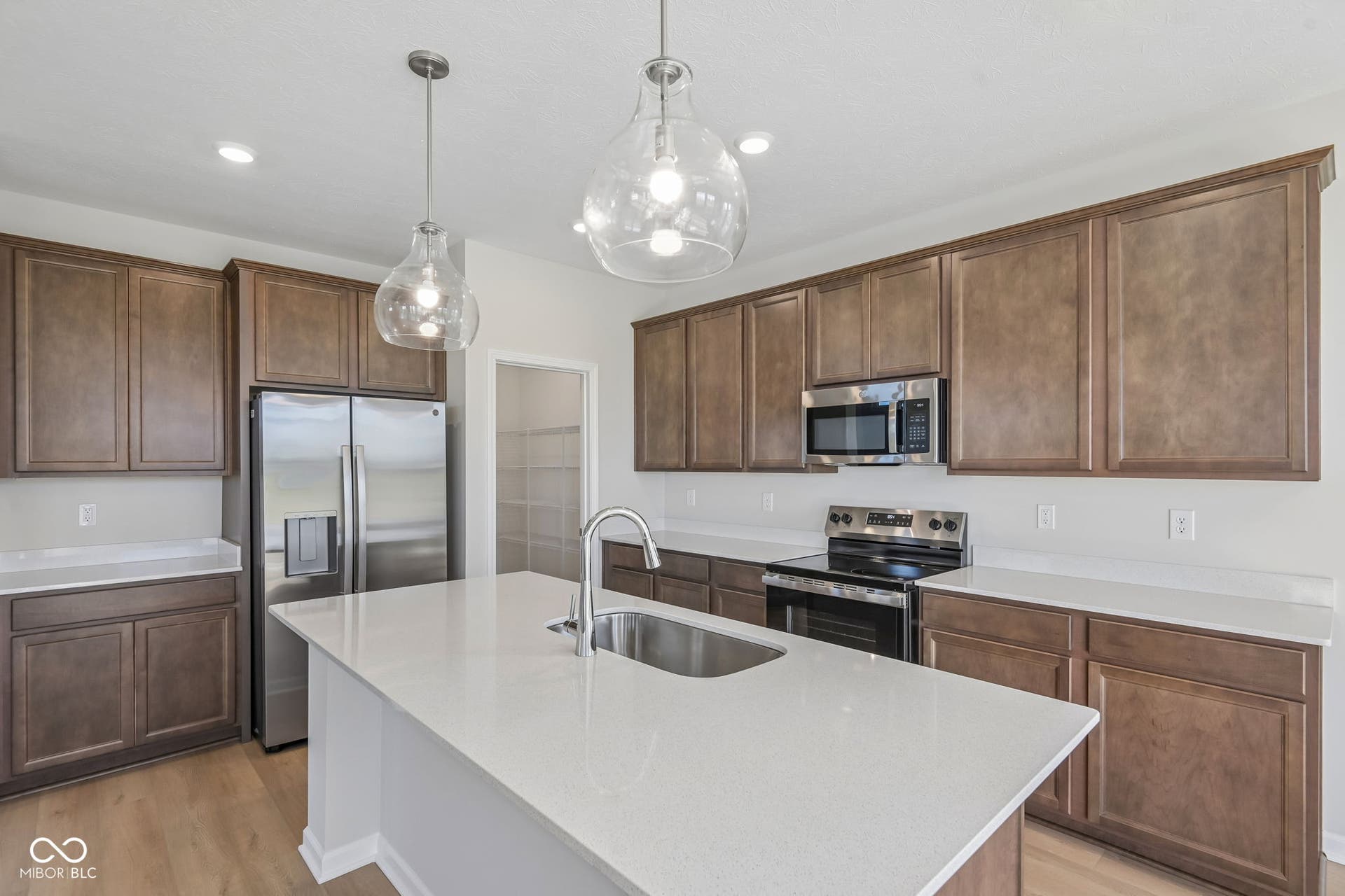 Modern kitchen featuring a large island with an undermount sink, stainless steel appliances, wood-finish flooring, recessed lighting, and clear glass pendant lights
