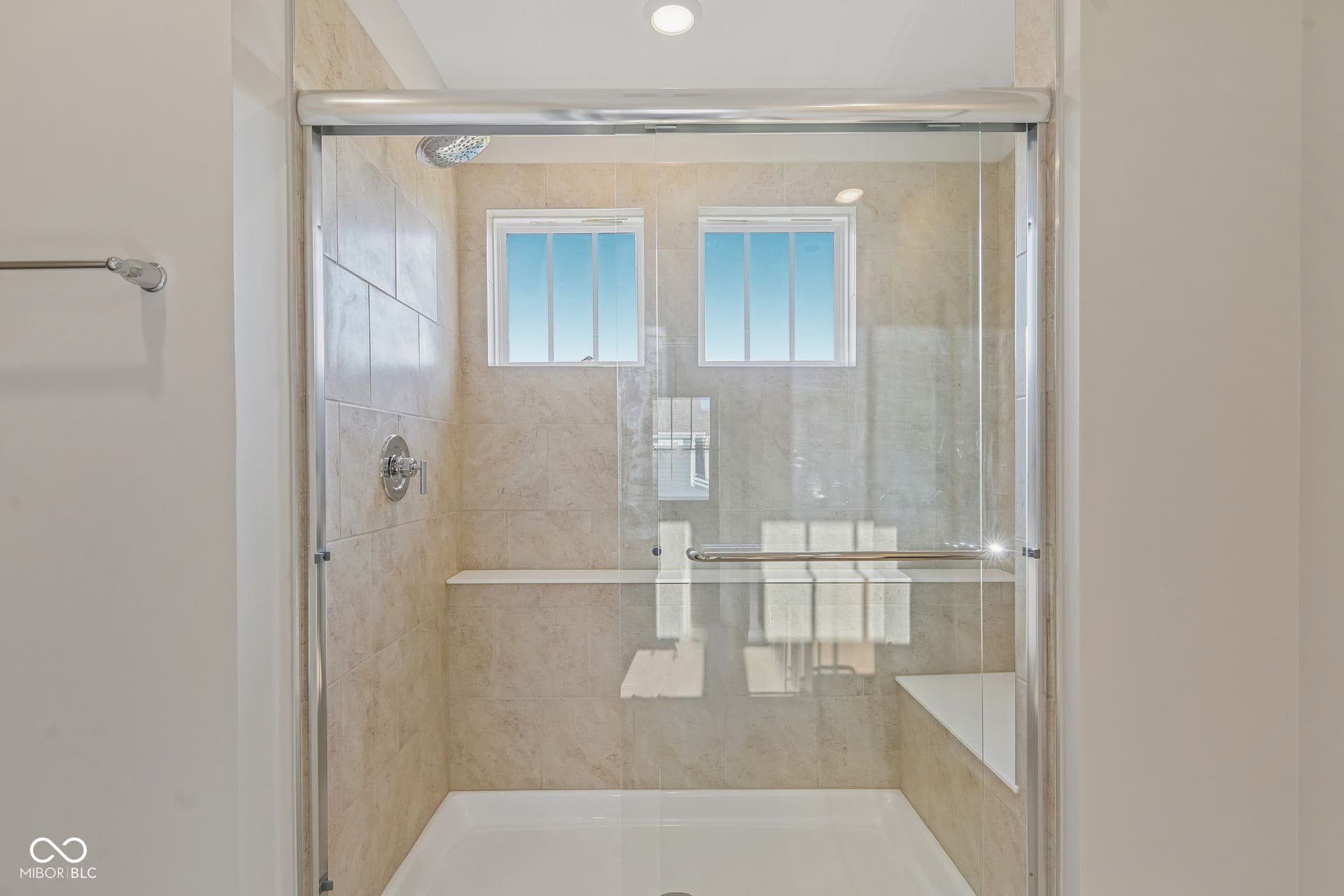 Glass-enclosed shower featuring light-toned tile surround, built-in shelving, integrated bench seating, two transom windows, and a rainfall showerhead