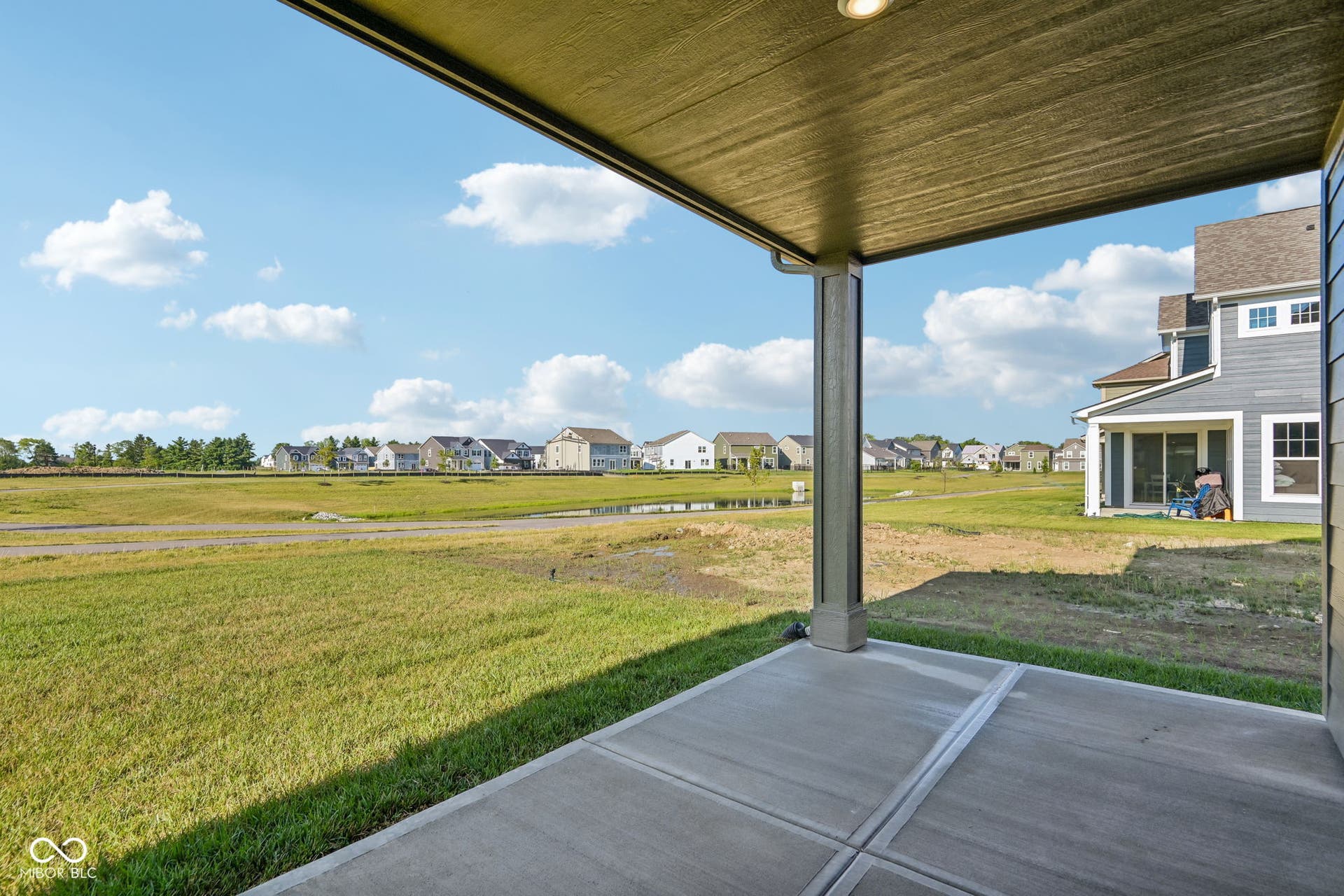 Covered concrete patio with recessed lighting, overlooking a green space and distant homes