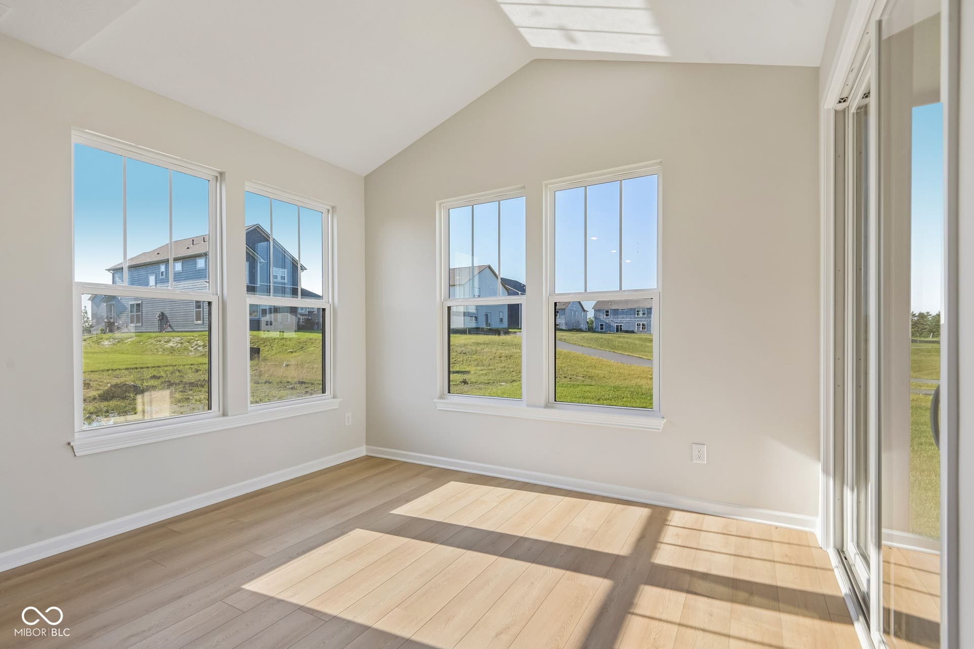 Bright sunroom with vaulted ceiling, multiple windows, light wood-finish flooring, and sliding glass doors