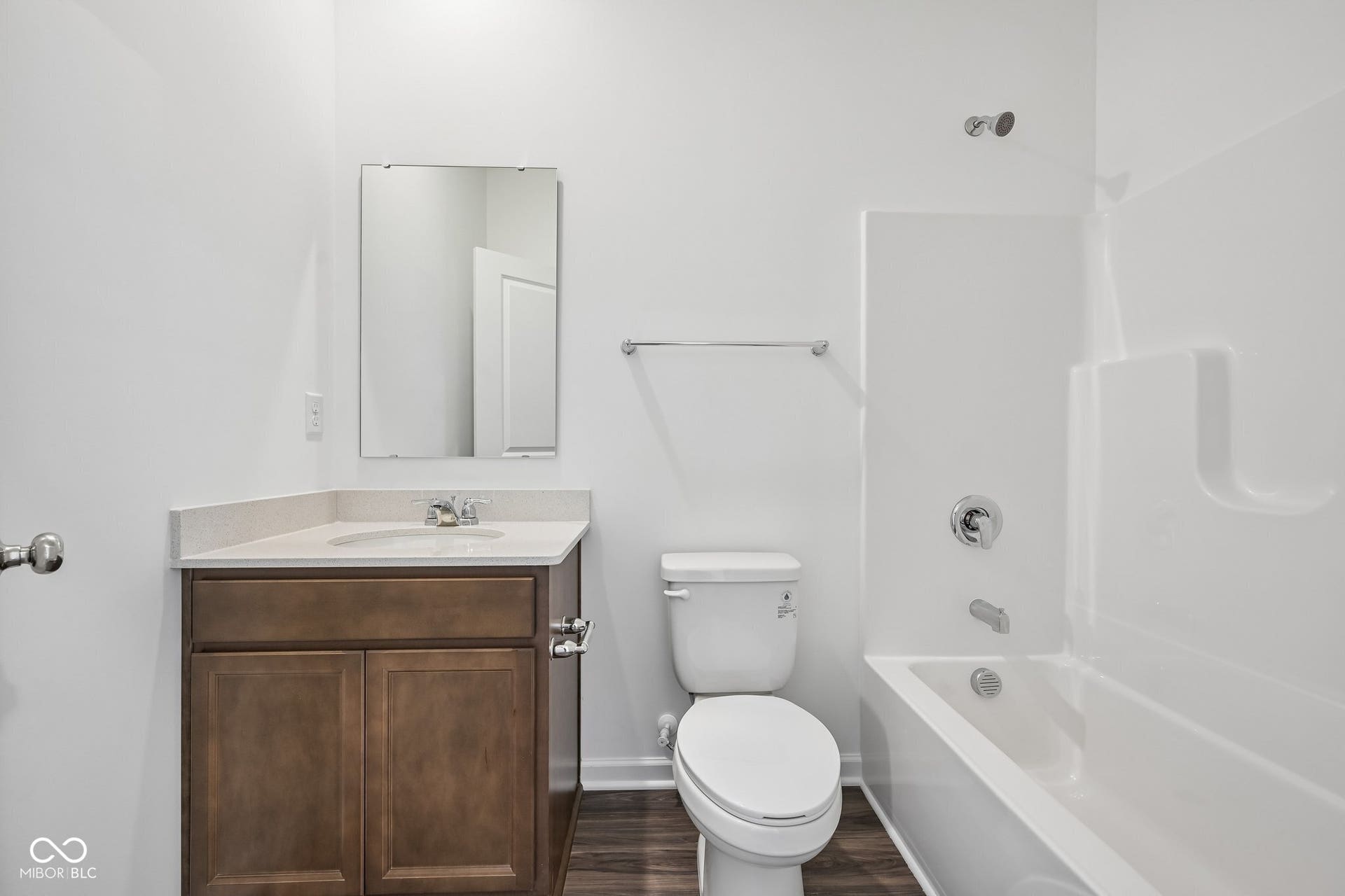 Wood-finish flooring, single vanity with light-toned countertop, rectangular sink, chrome faucet, and a combination shower/tub