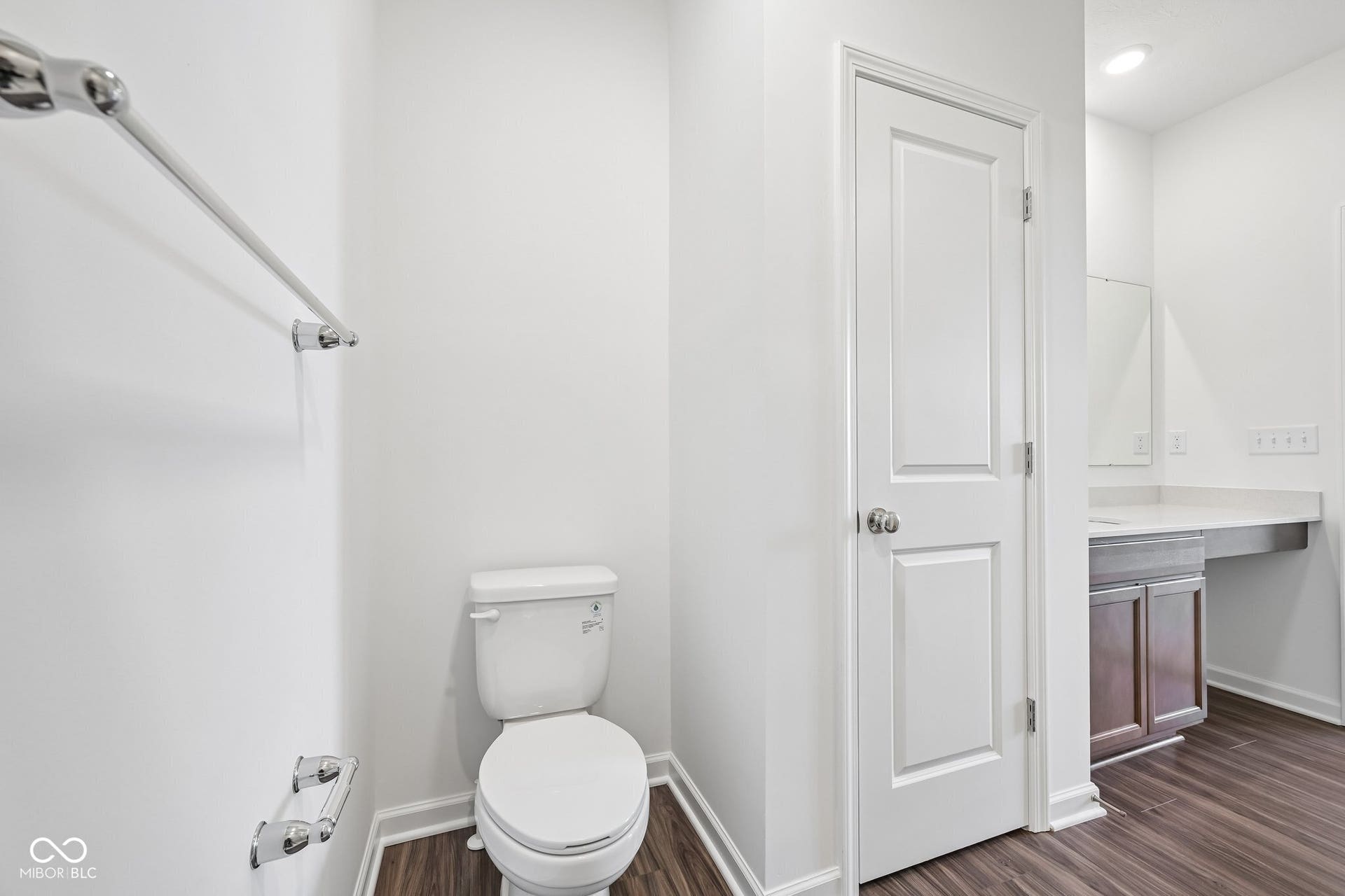 Compact bathroom featuring a white ceramic toilet, chrome fixtures, and wood-finish flooring