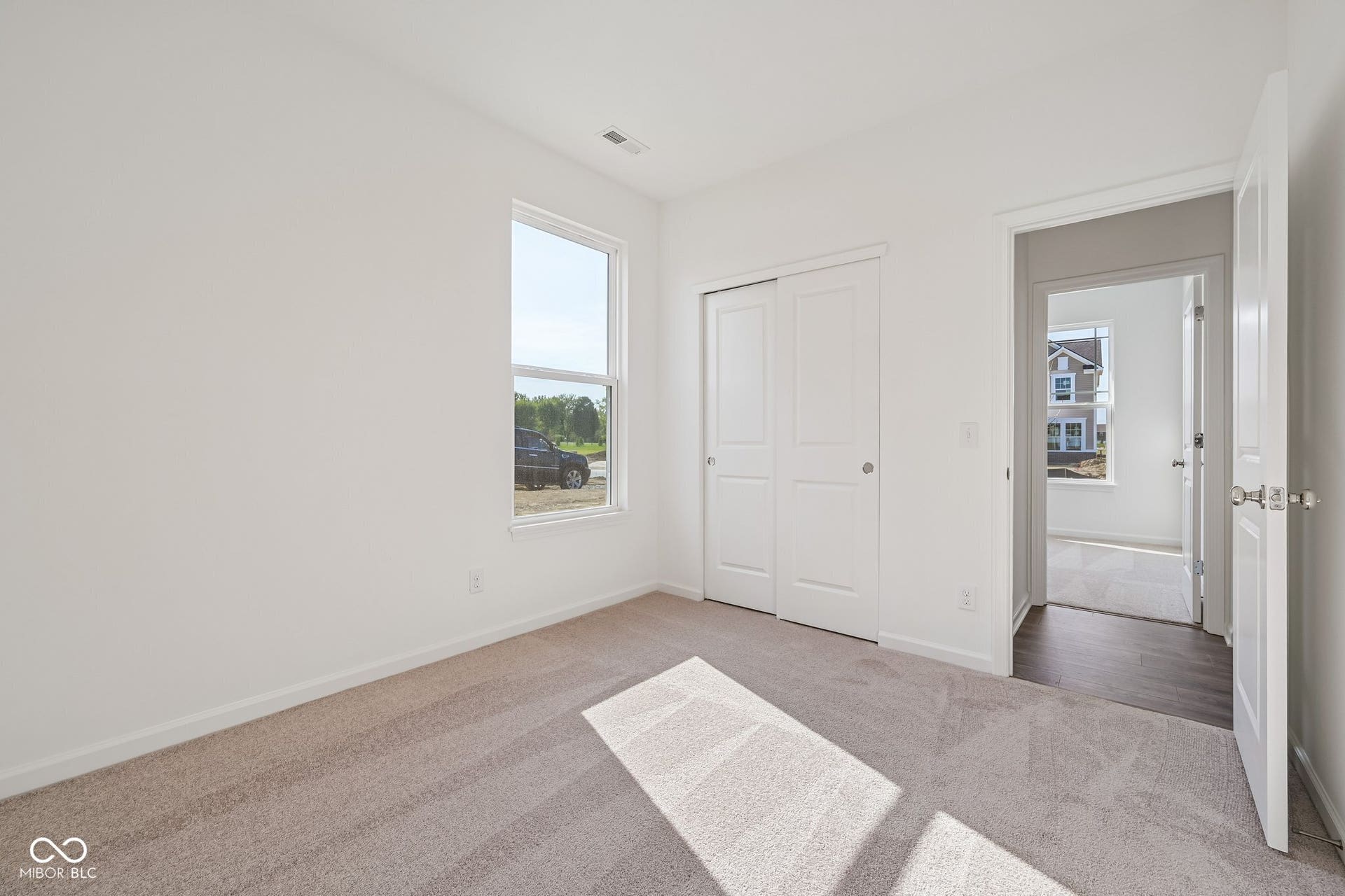 Light-toned carpeted flooring, white walls, a window with white trim, and a double-door closet with white paneled doors