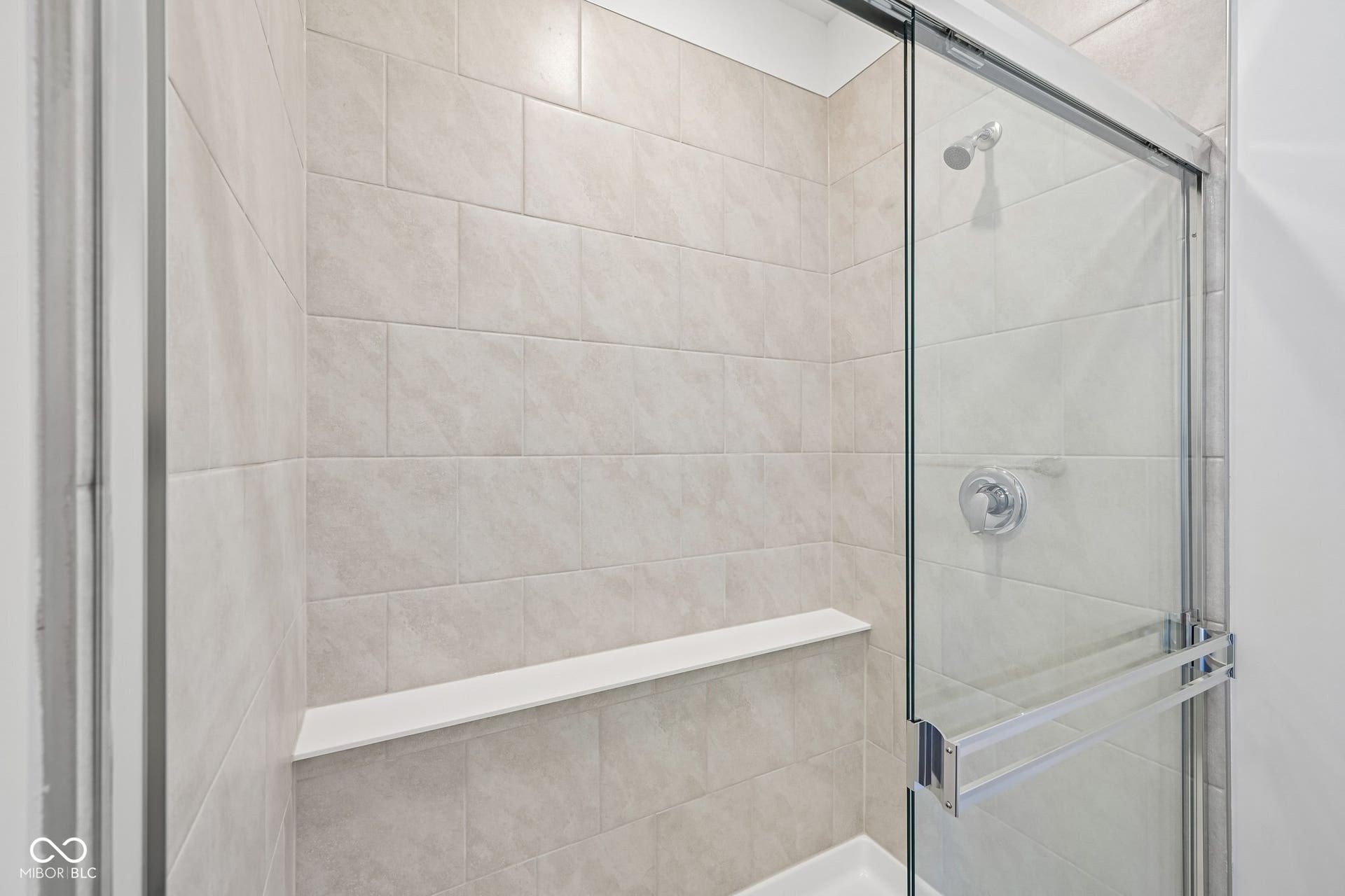 Tiled shower enclosure featuring a built-in bench, chrome fixtures, and a glass sliding door