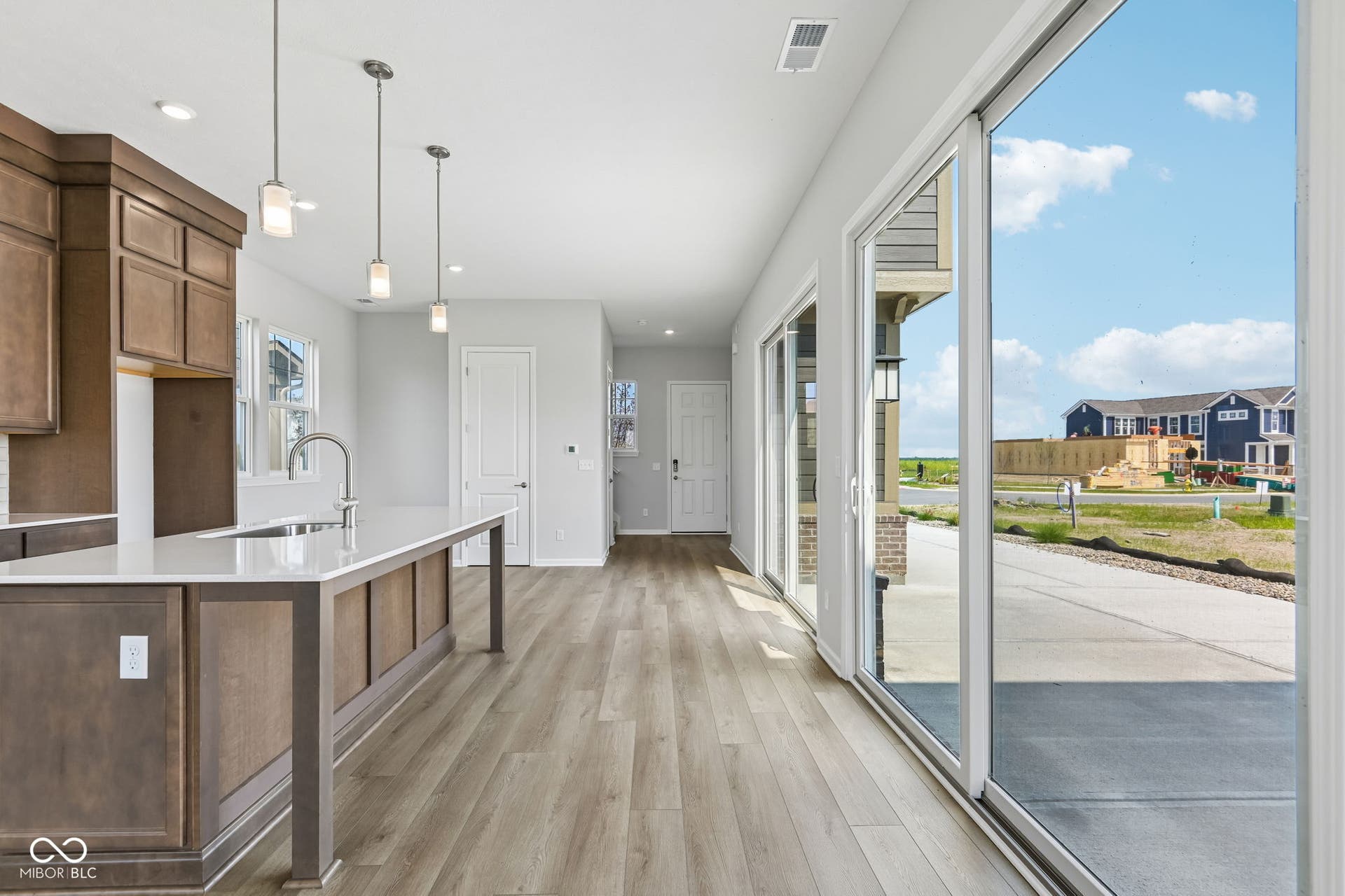 15762 Showdown Road, Noblesville, IN 46060 Open-concept interior featuring light wood-finish flooring, a kitchen island with a single-basin sink, pendant lighting, and full-height sliding glass doors