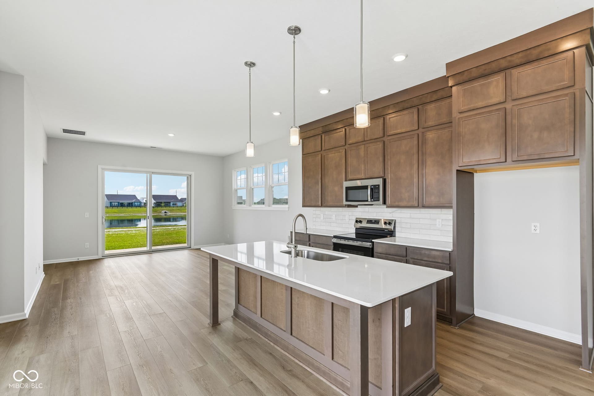 15762 Showdown Road, Noblesville, IN 46060 Open concept kitchen and living area featuring wood-finish flooring, a kitchen island with a white solid surface countertop, dark wood cabinetry, a subway tile backsplash, and stainless steel appliances