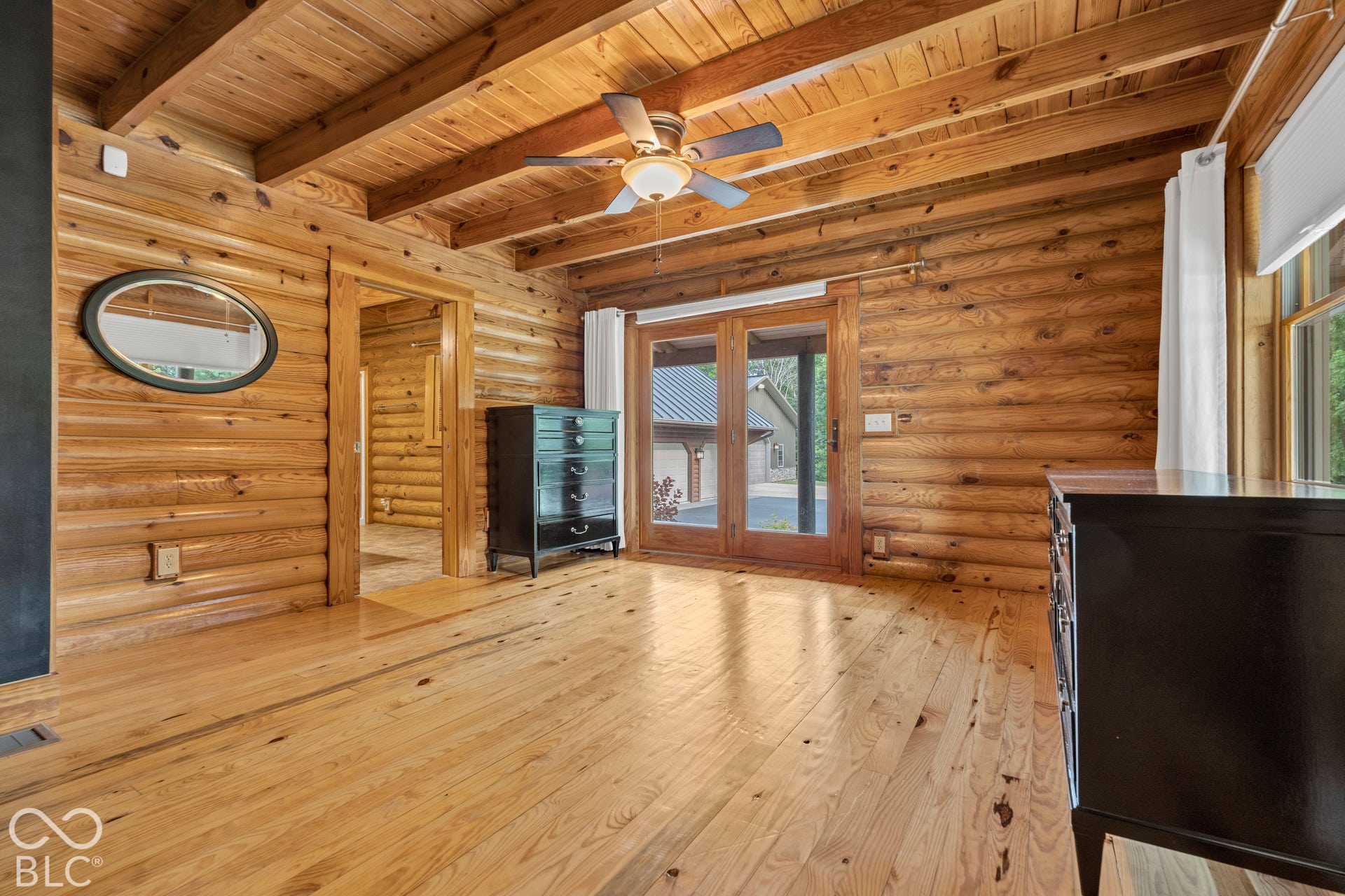 Wood-paneled walls and ceiling, exposed wood beams, wood-finish flooring, ceiling fan with integrated lighting, glass panel doors