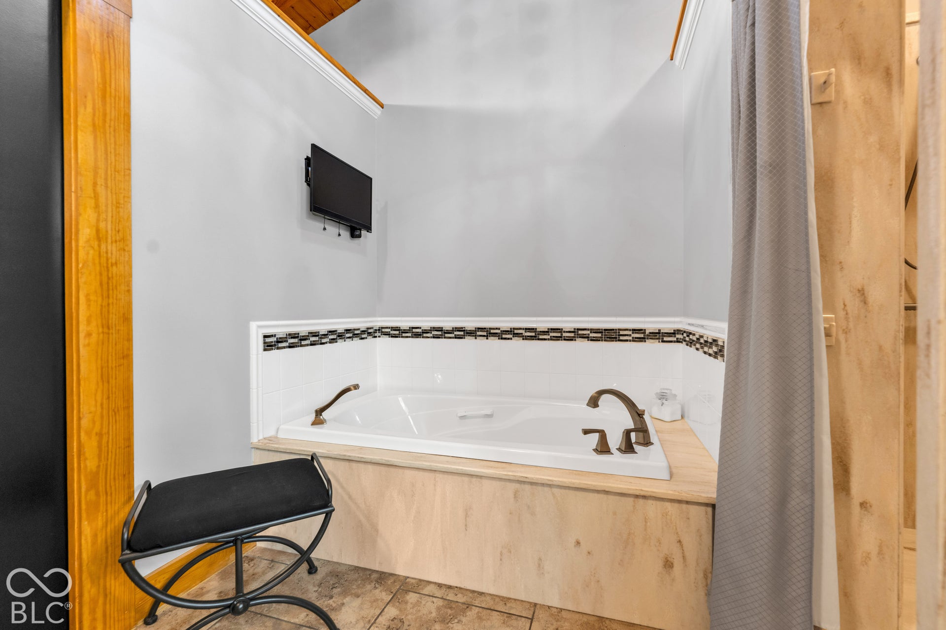 White soaking tub with mosaic tile detailing and bronze-finish fixtures