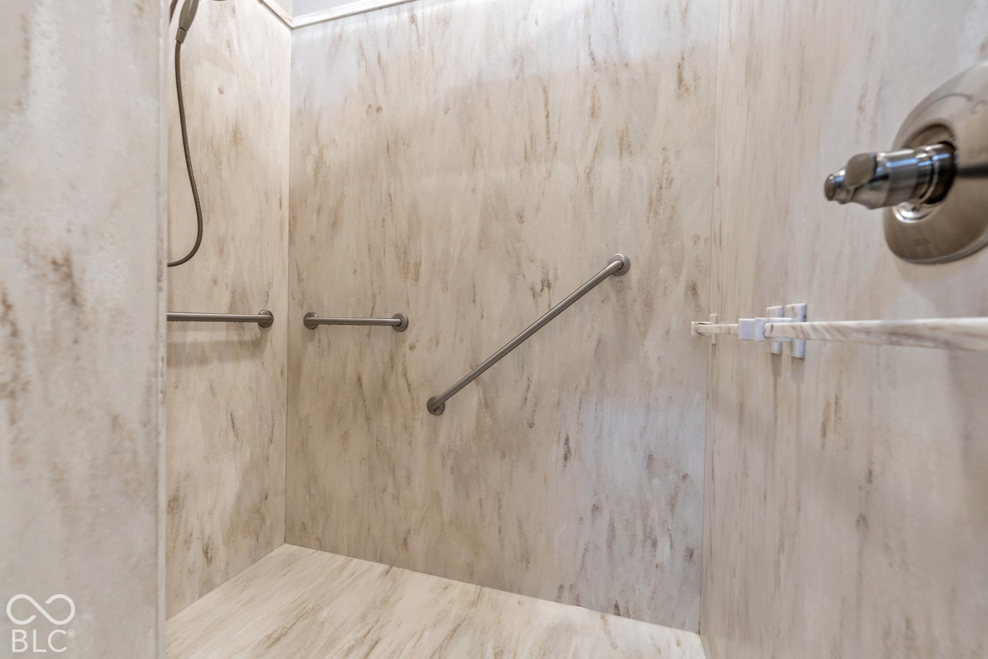 Walk-in shower with integrated grab bars, patterned wall panels, and a handheld shower fixture