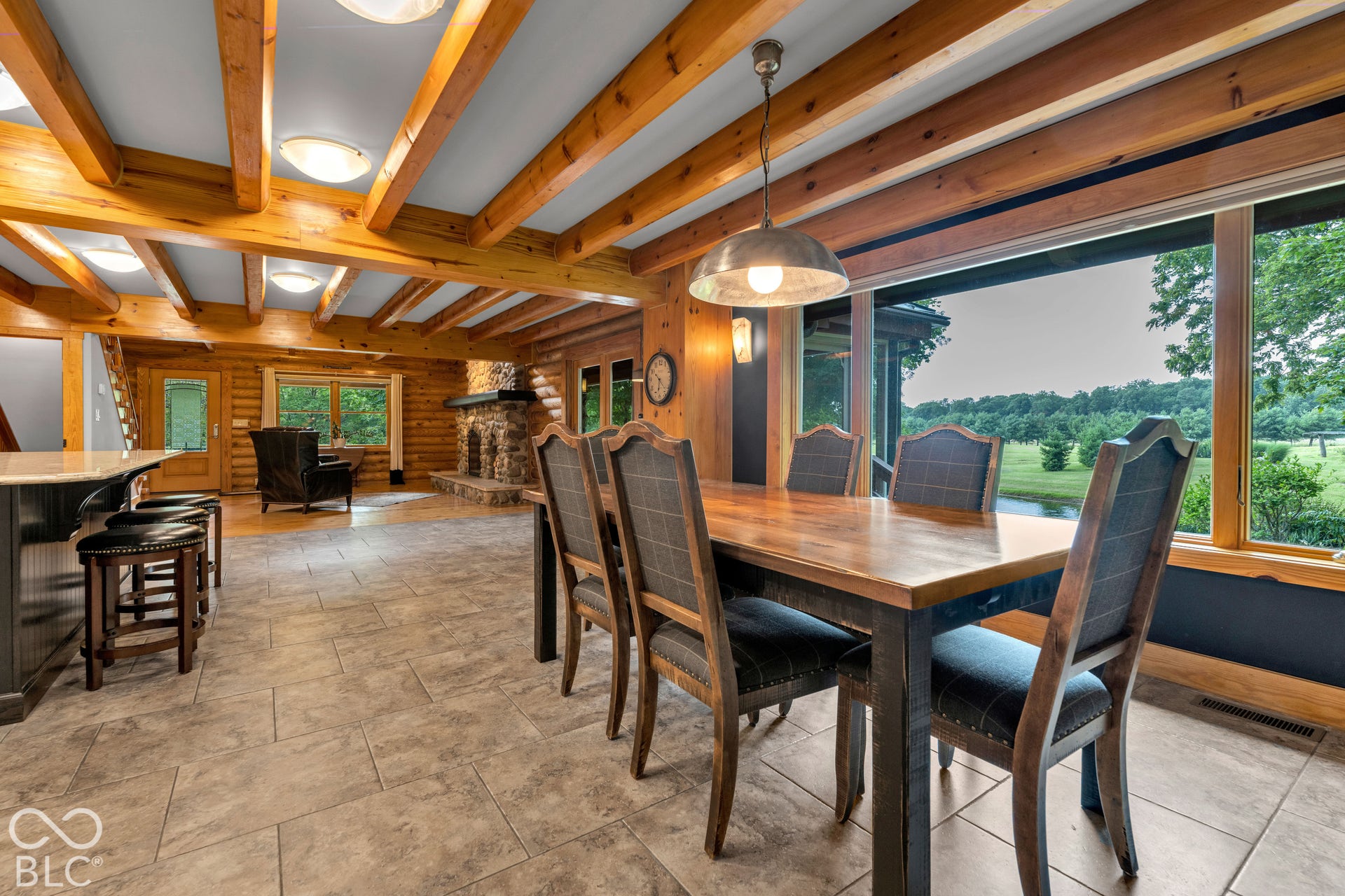 Exposed wood beam ceilings, large format tile flooring, stone-clad fireplace, built-in breakfast bar, and expansive picture windows
