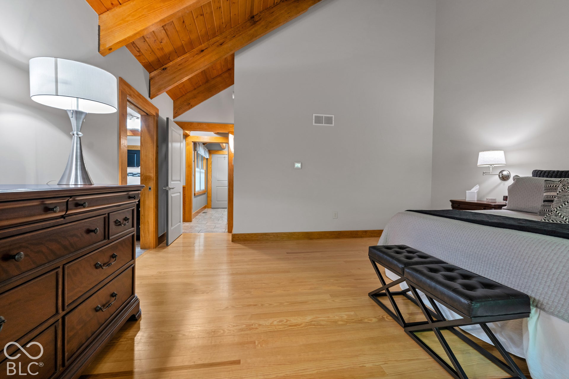 Vaulted wood-beamed ceiling, natural wood flooring, wood trim, and wall-mounted lighting