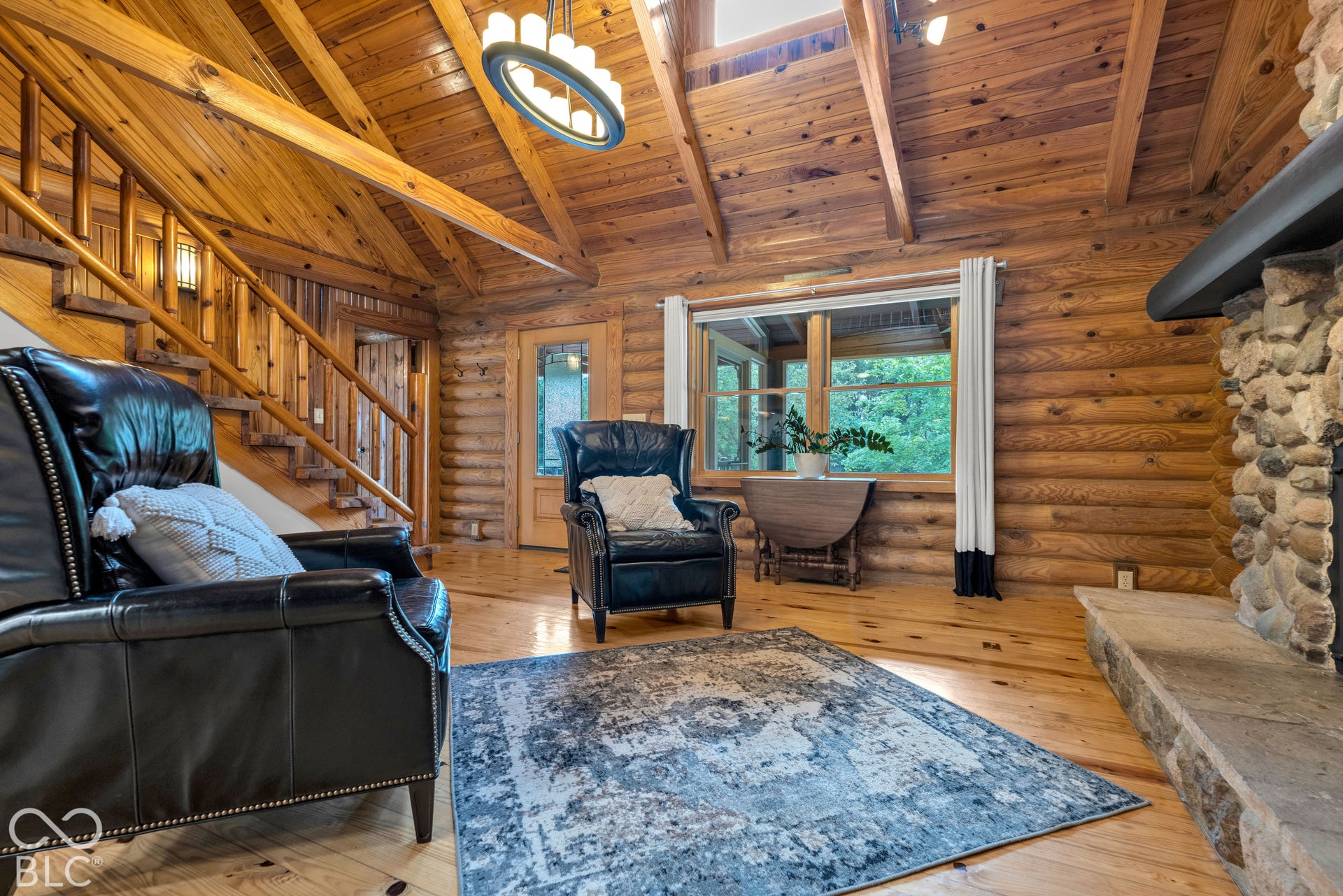 Vaulted wood-paneled ceilings with exposed beams, wood-finish flooring, a stone fireplace, and a wood staircase with log railings