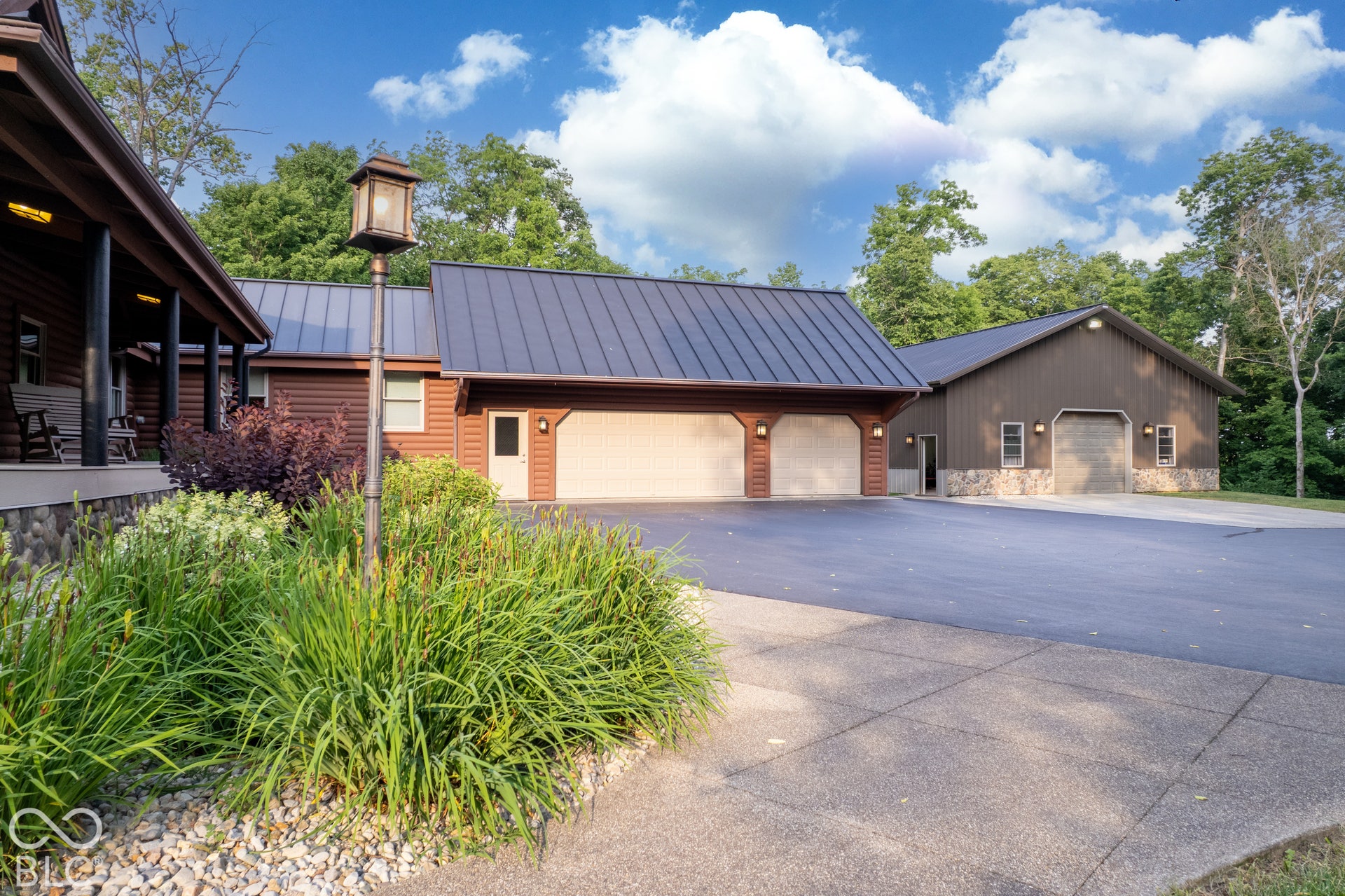 Multiple structures featuring a paved driveway, a large garage with two roll-up doors, and an additional outbuilding with stone veneer accents