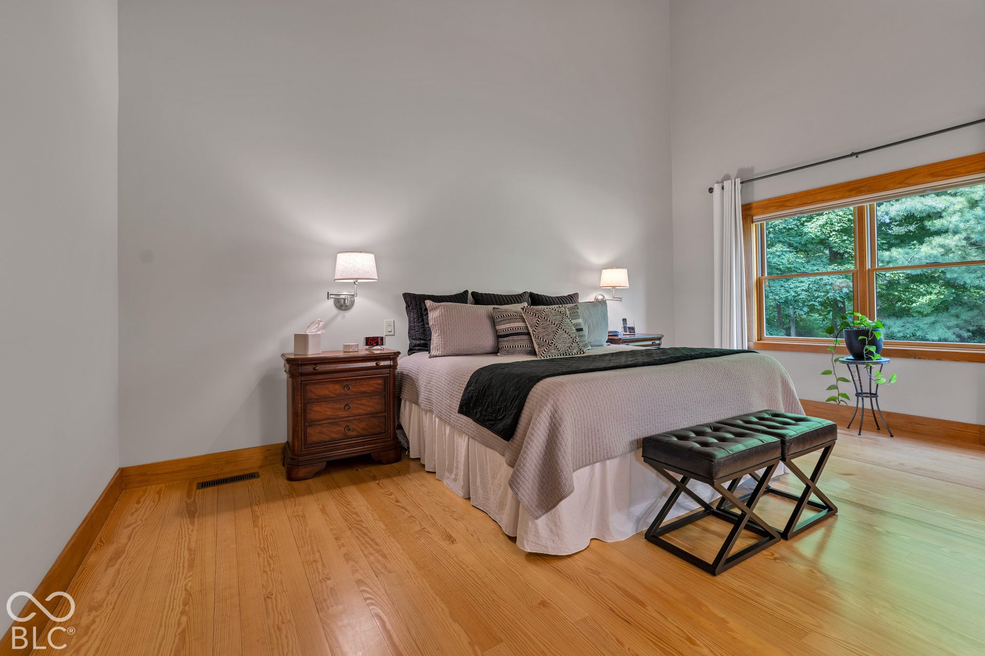 Hardwood flooring, large window with wood trim, wall-mounted sconce lighting, and high ceilings