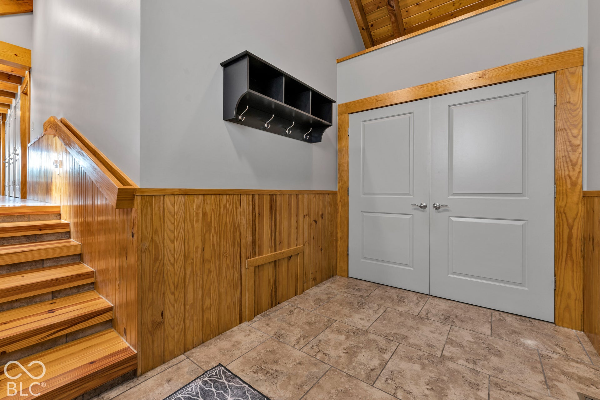 Warm wood paneling, wood-finish staircase, and light gray paneled double doors