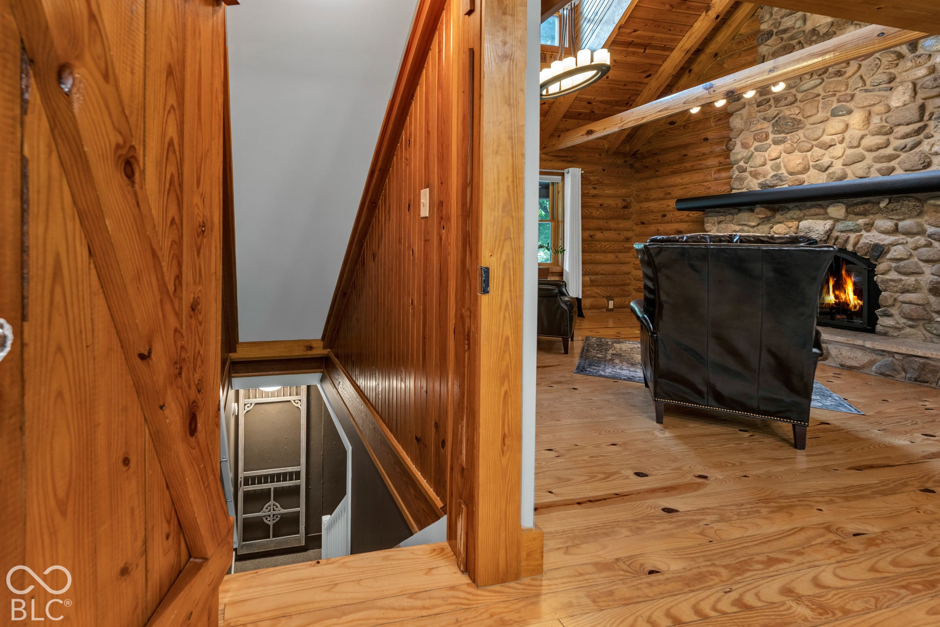 Wood-finish flooring, log wall construction, stone-clad fireplace with mantel, and exposed wood ceiling beams