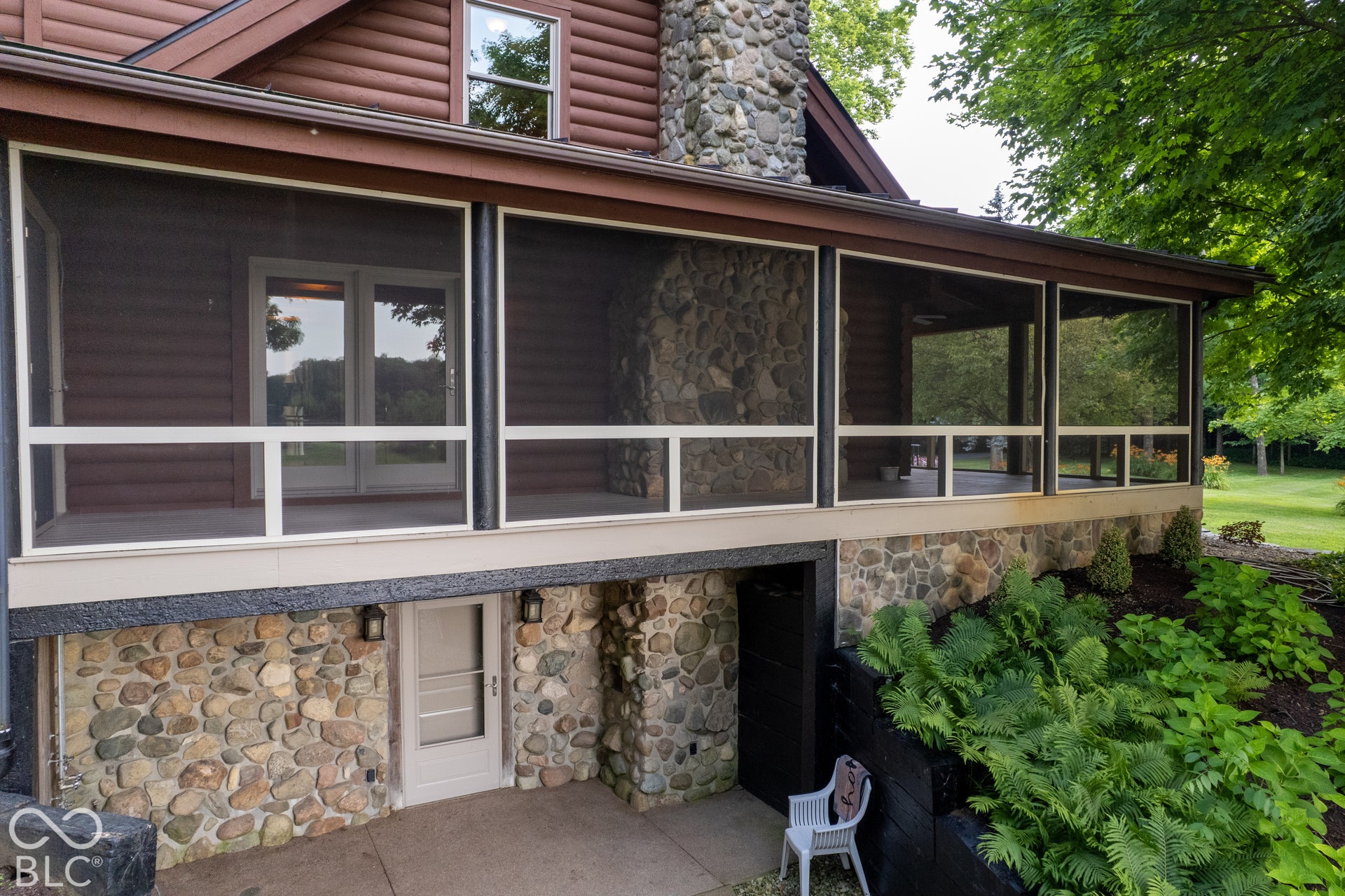 Lower level stone facade, screened porch, double glass doors, stone chimney, and exterior lighting