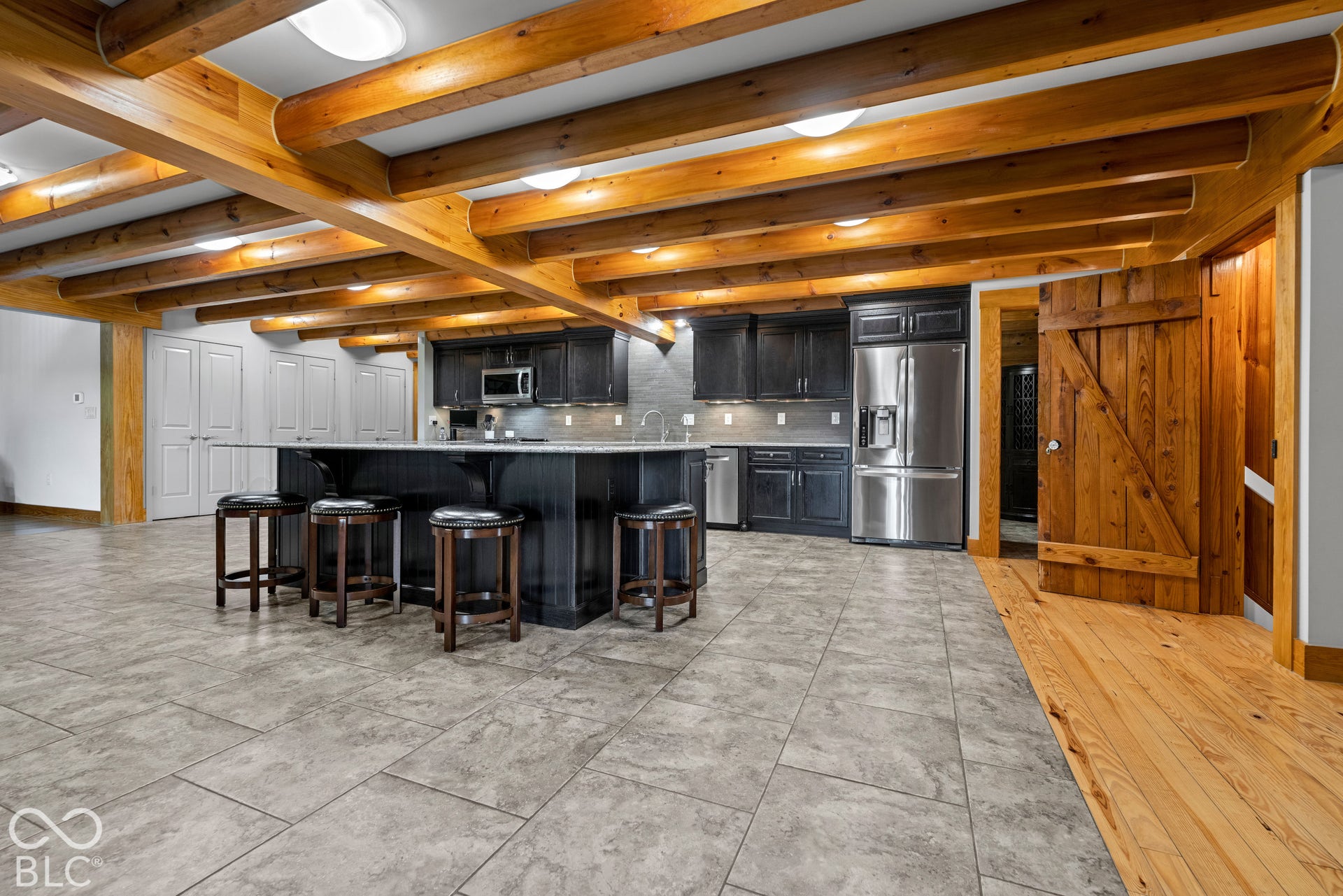 Exposed wood beams, integrated kitchen island with seating, dark wood cabinetry, stainless steel appliances, and tiled flooring