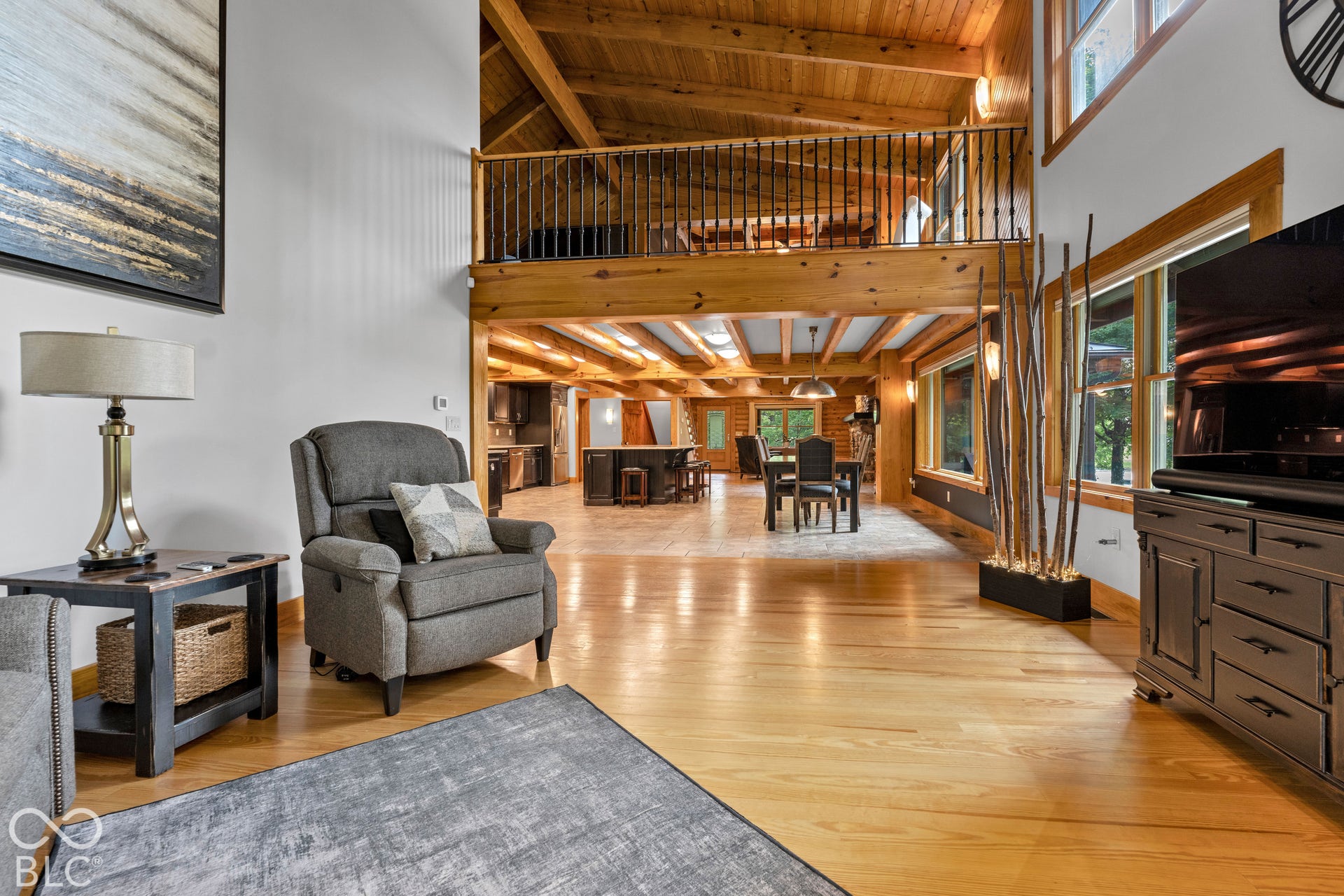 Vaulted wood-paneled ceilings with exposed beams, wood-finish flooring, an open-concept layout, a balcony with metal railings, and extensive window features