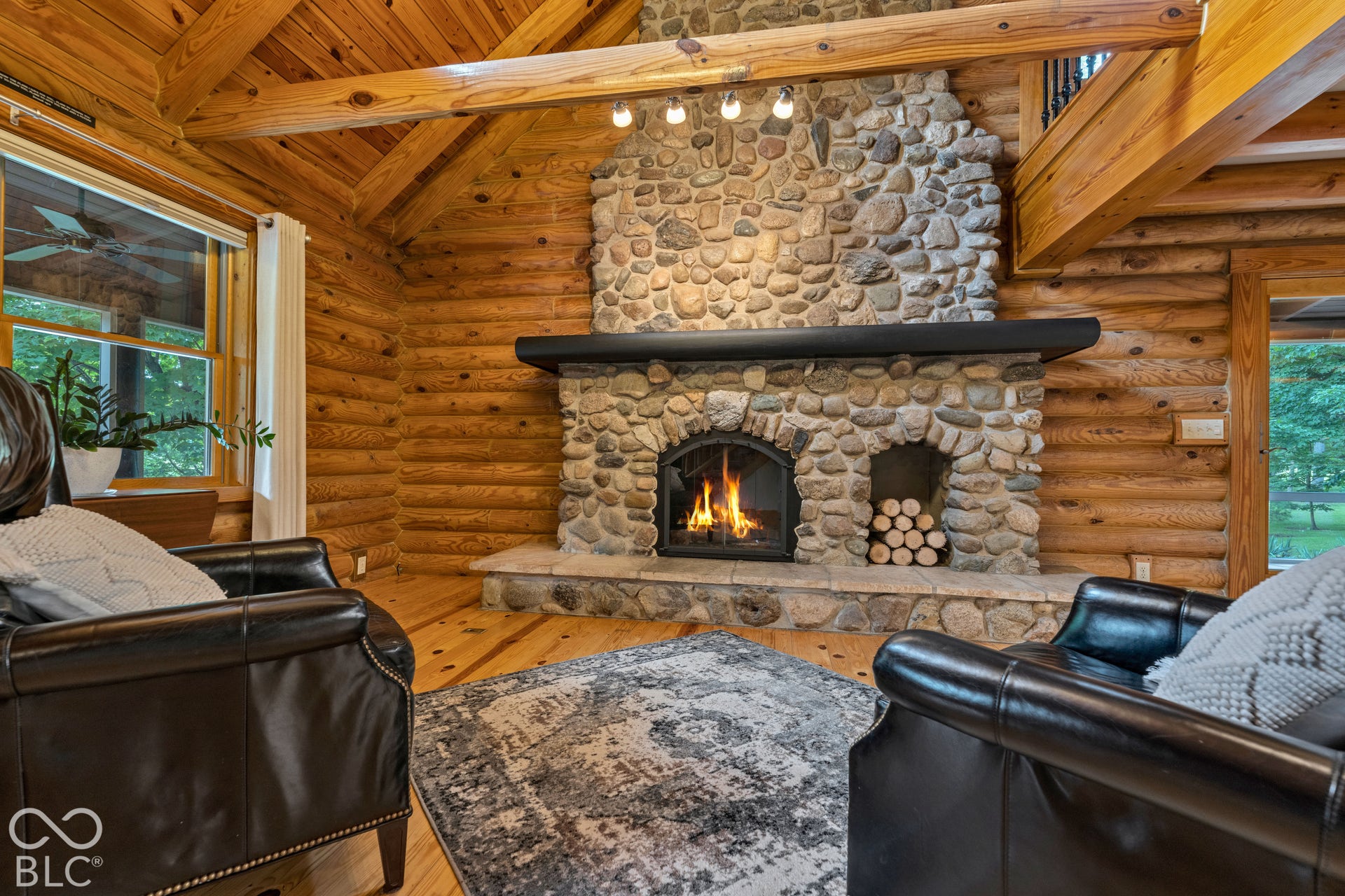 Log cabin interior featuring a stone fireplace with a built-in wood storage niche, exposed wood beam ceiling, wood-finish flooring, and log walls
